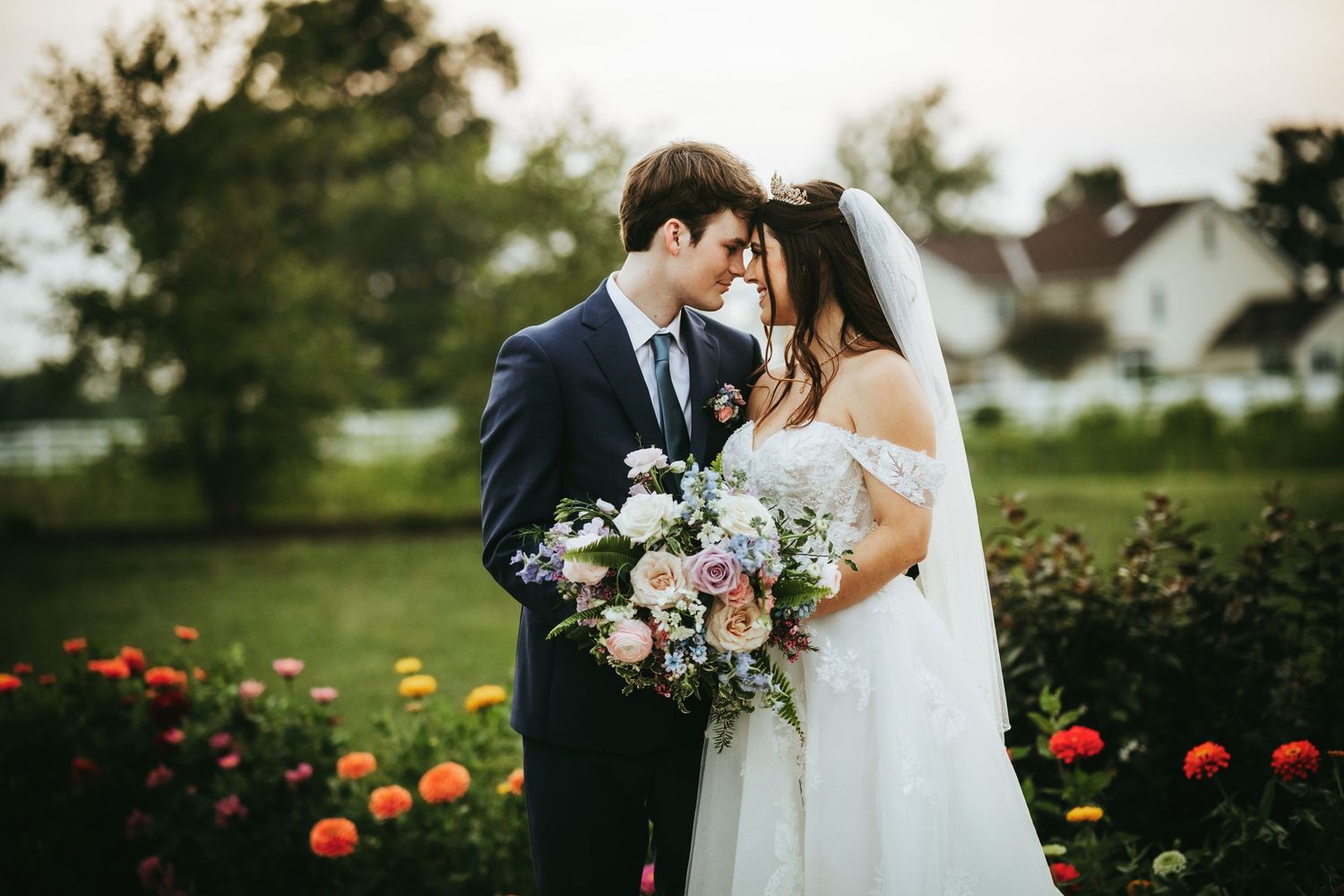 Newlywed couple shares intimate moment in garden with colorful flowers and bouquet at sunset.