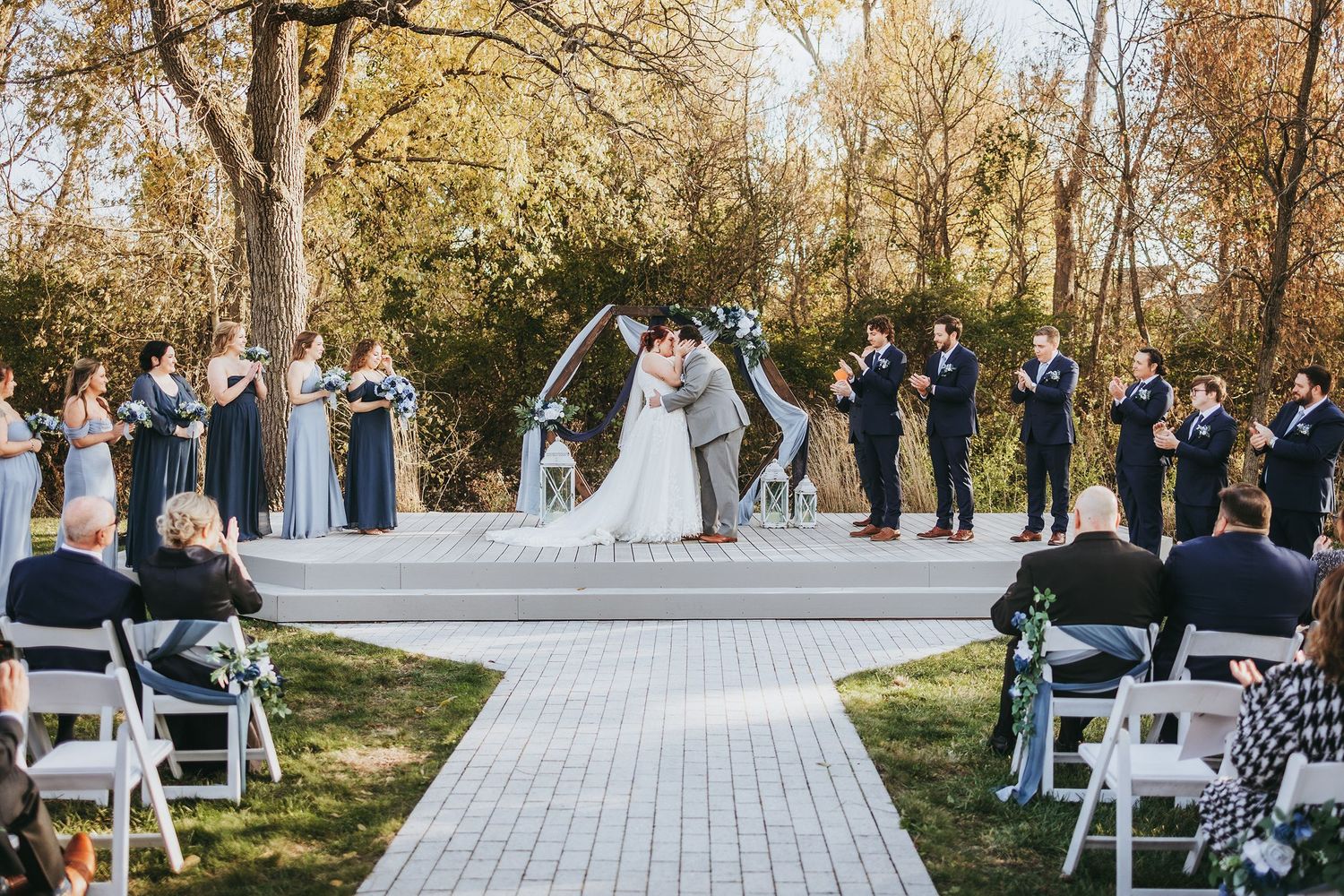 Outdoor wedding ceremony setup with white chairs and natural fall foliage.