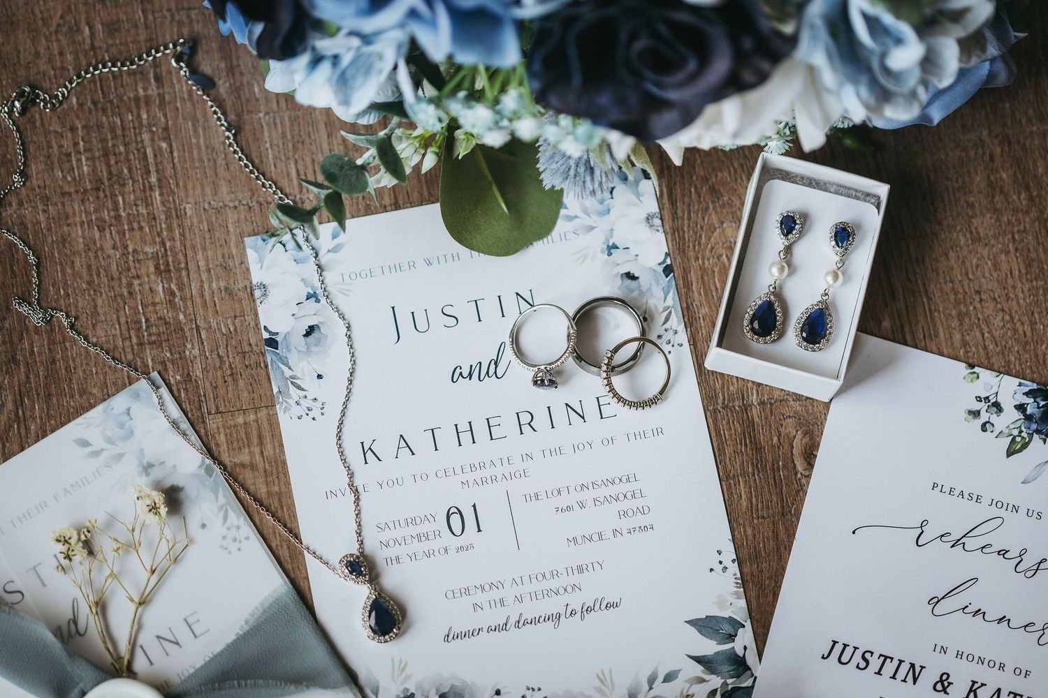 Wedding invitation suite with floral details and rings styled on rustic wooden surface.