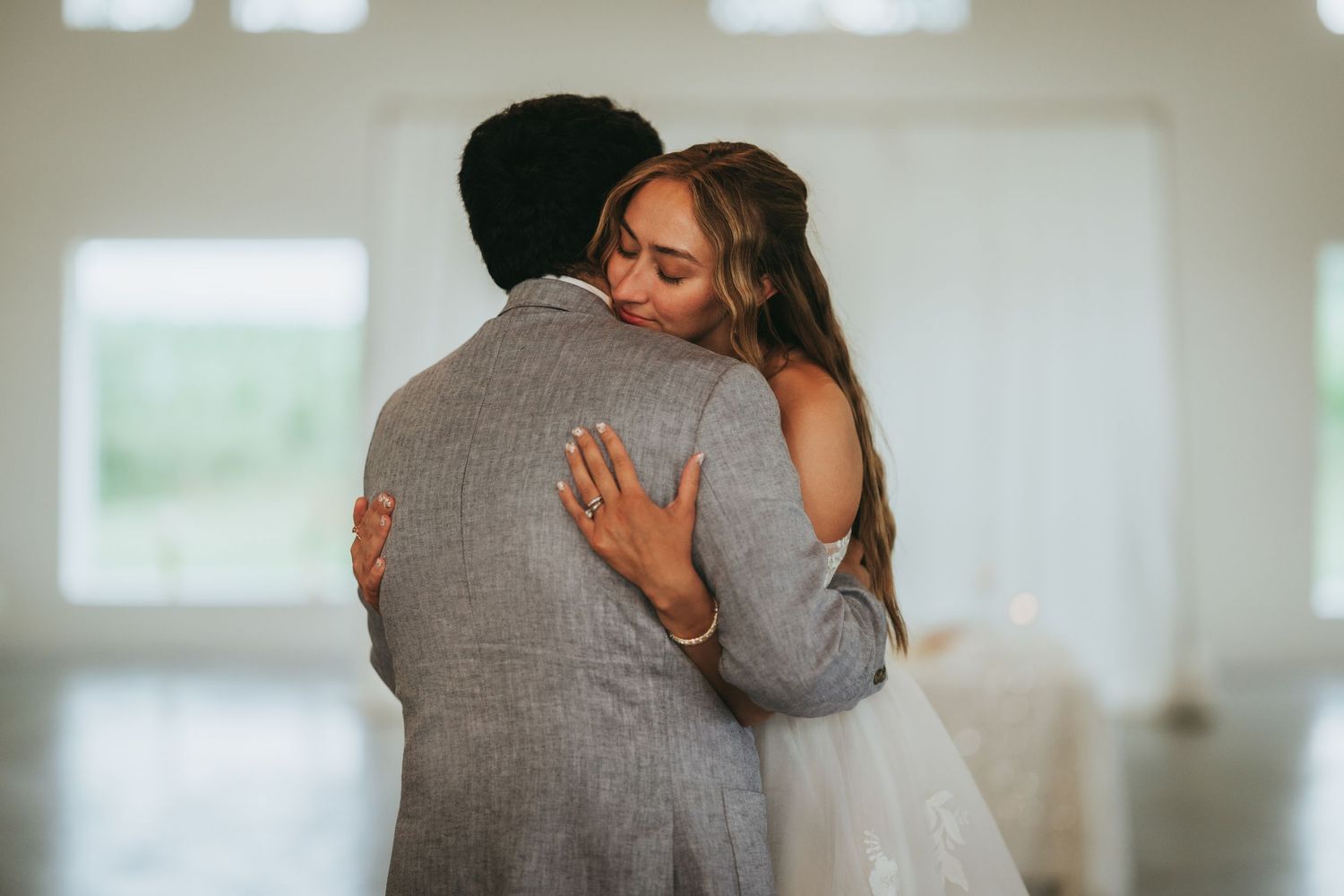 Bride and groom share an emotional first dance embrace in a bright, airy wedding venue.