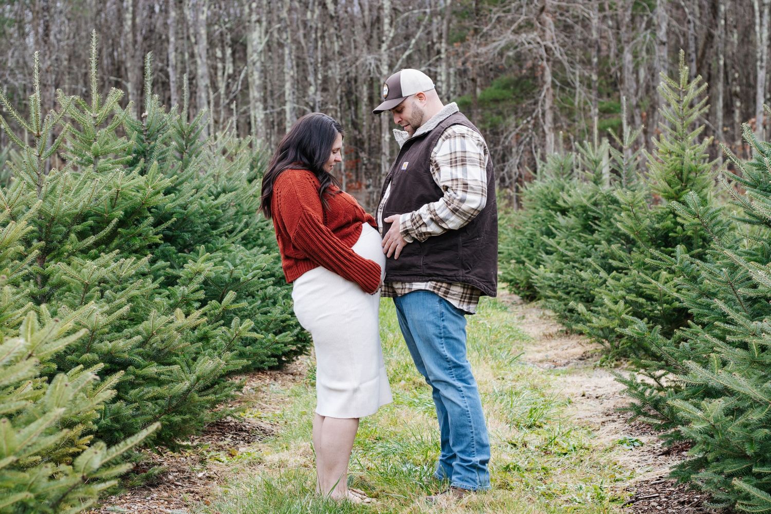 Romantic winter engagement photos captured between evergreen trees in a snowy forest setting.