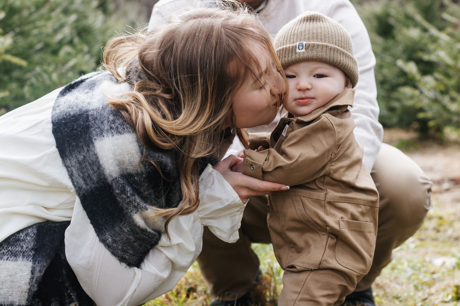 Tender winter moments captured among snow-dusted evergreen trees at a Christmas tree farm.