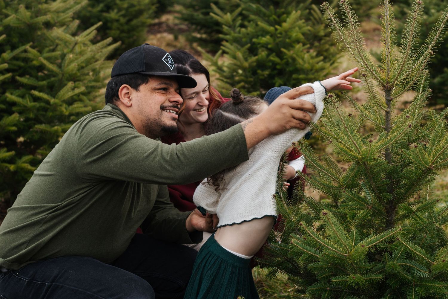 Family enjoying a winter day together at a Christmas tree farm surrounded by evergreens.