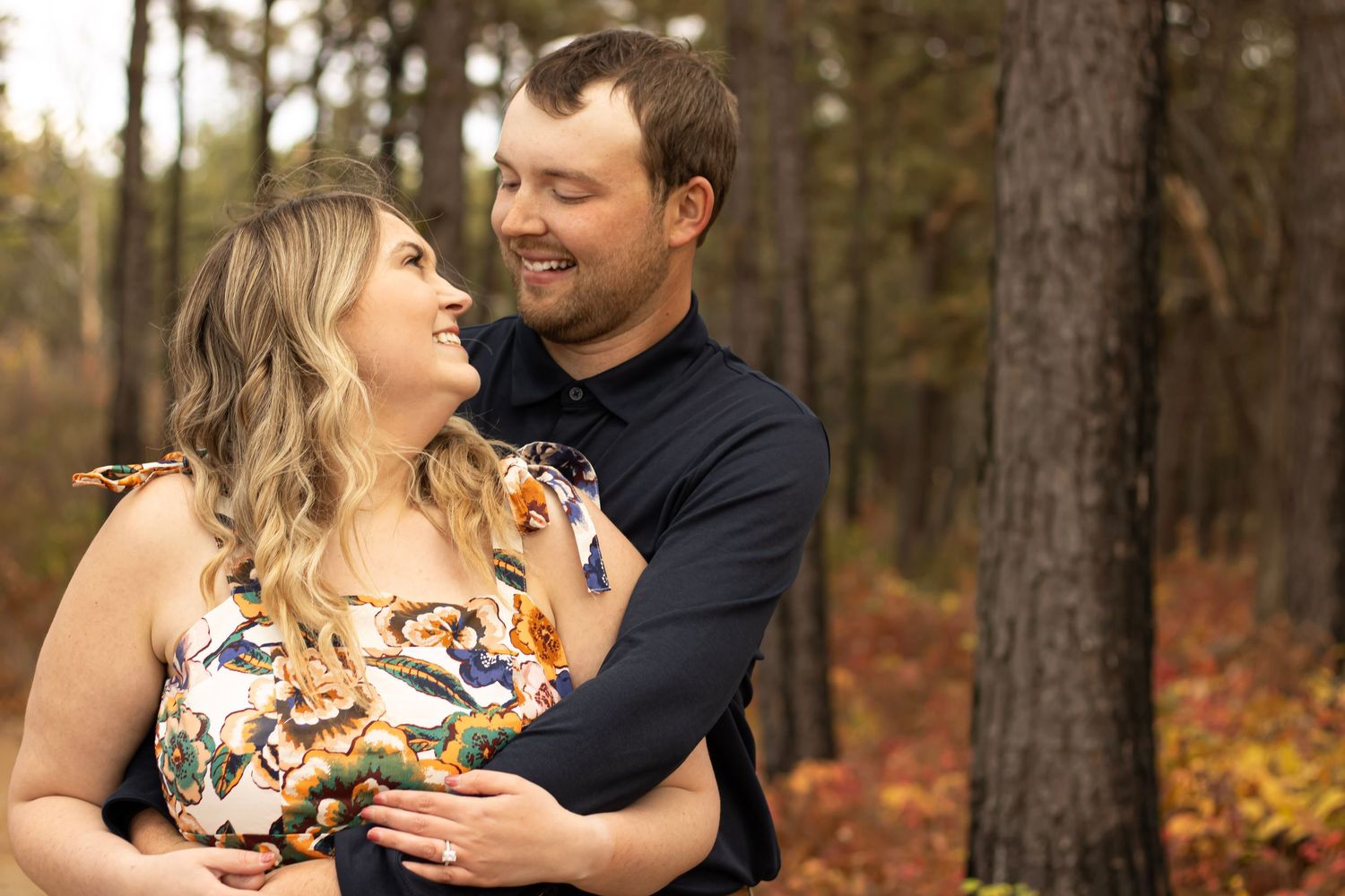 Couple sharing intimate moments during outdoor autumn photoshoot in wooded setting.