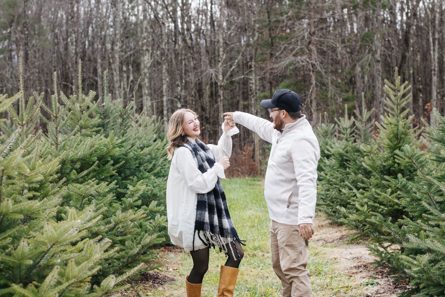 Couple walking hand in hand through rows of evergreen trees at Christmas tree farm.