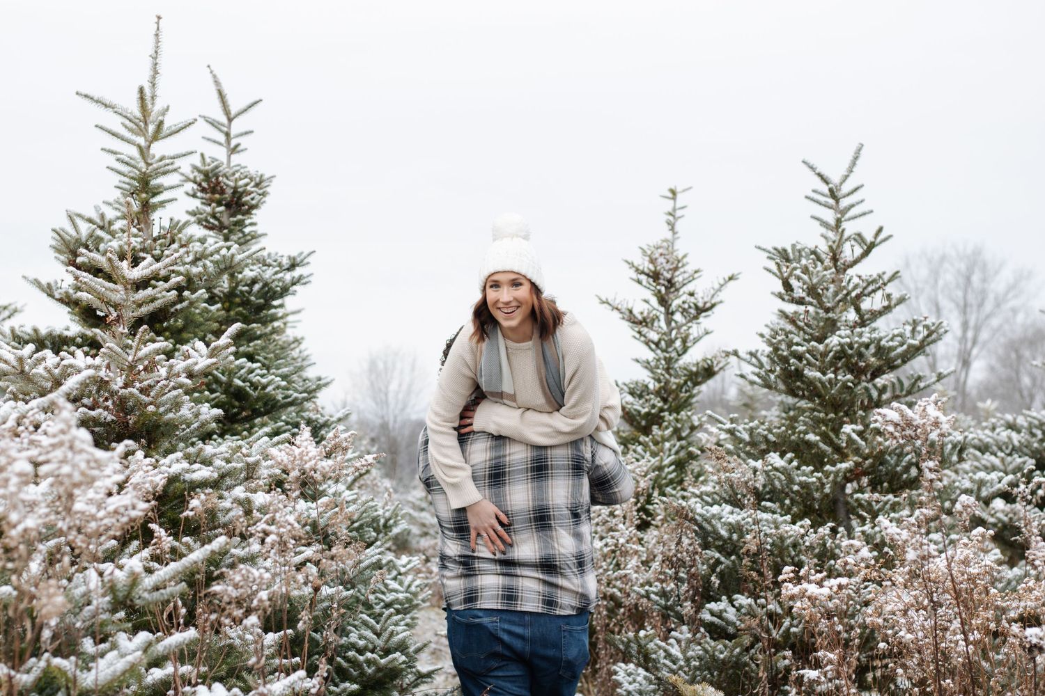 Couple shares intimate moments between snow-covered pine trees at a festive Christmas tree farm.