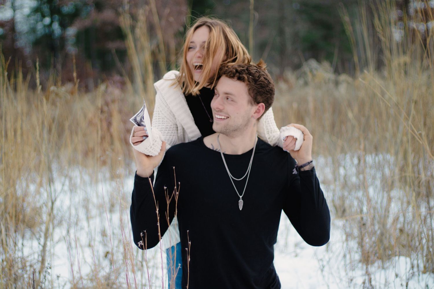 Joyful couple laughing together during winter photoshoot in snowy field.