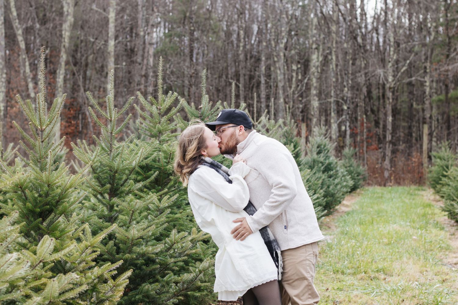 A romantic winter engagement photoshoot among snow-dusted evergreen trees at a Christmas tree farm.