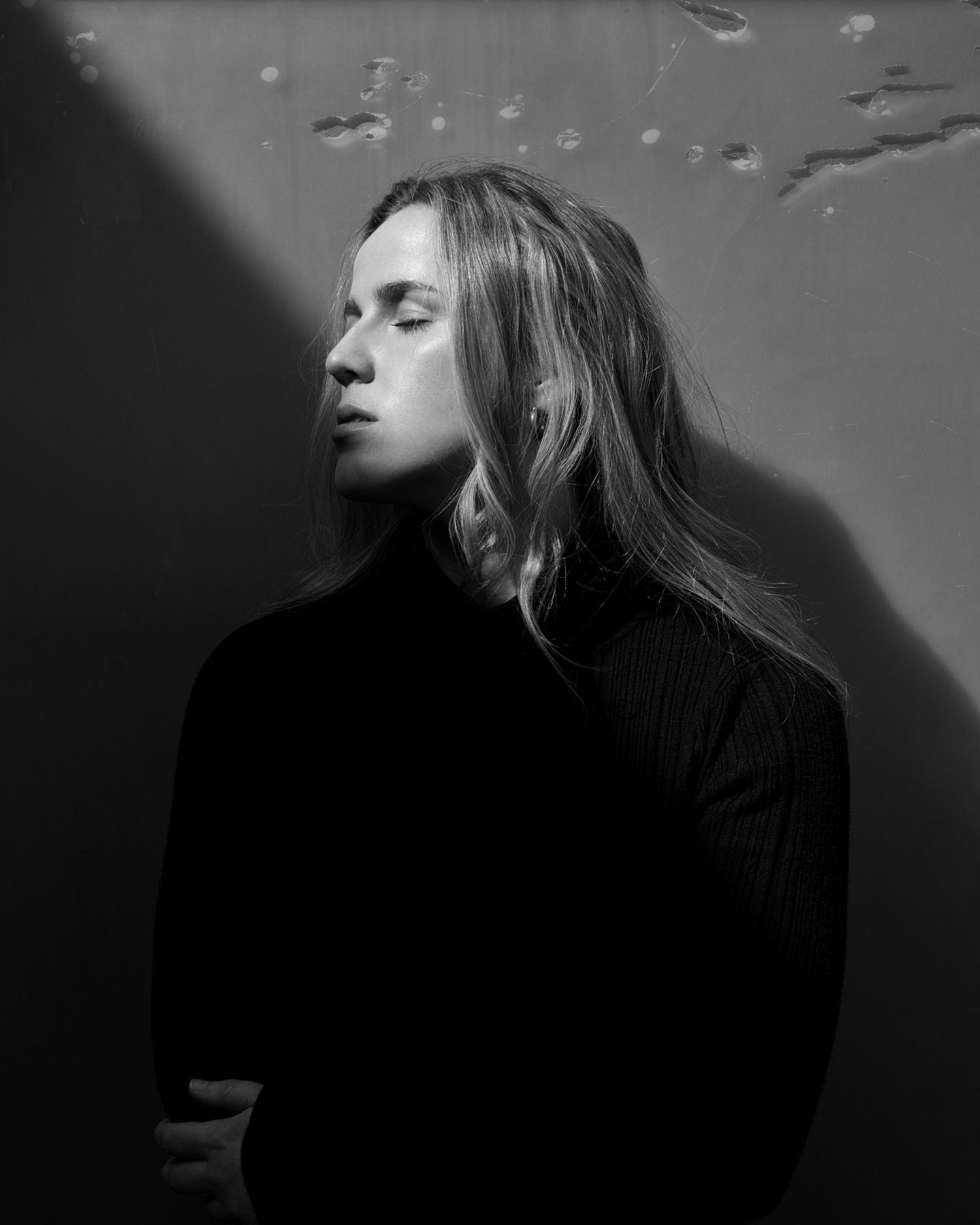 Dramatic black and white portrait of a person in a black turtleneck with flowing hair against a shadowed background.