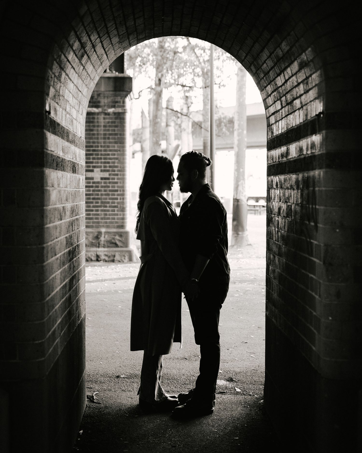 A black and white photos showing silhouettes of two people standing in a dark brick tunnel.