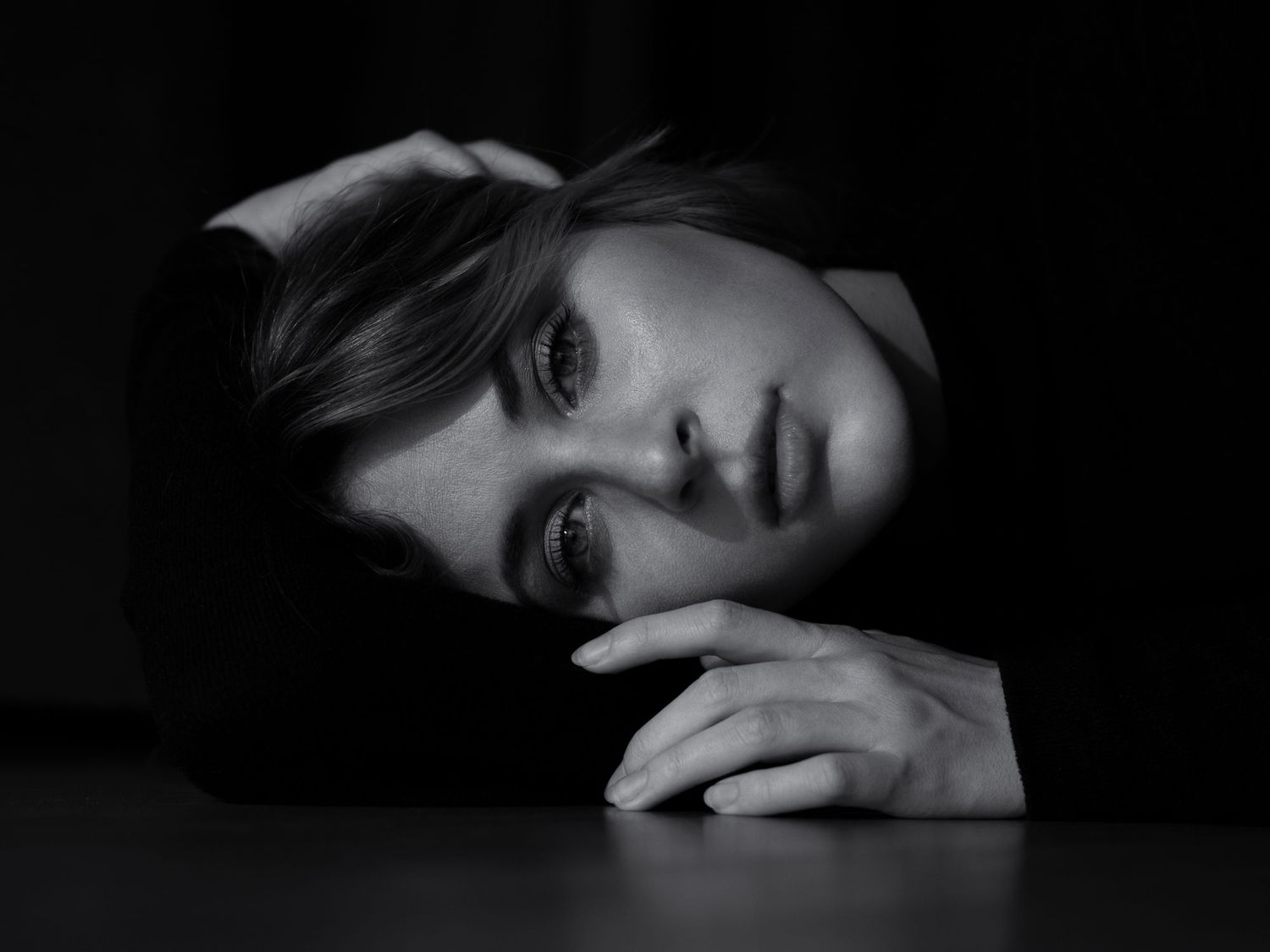 A dramatic black and white portrait showing an intense gaze and resting hand against a dark background.