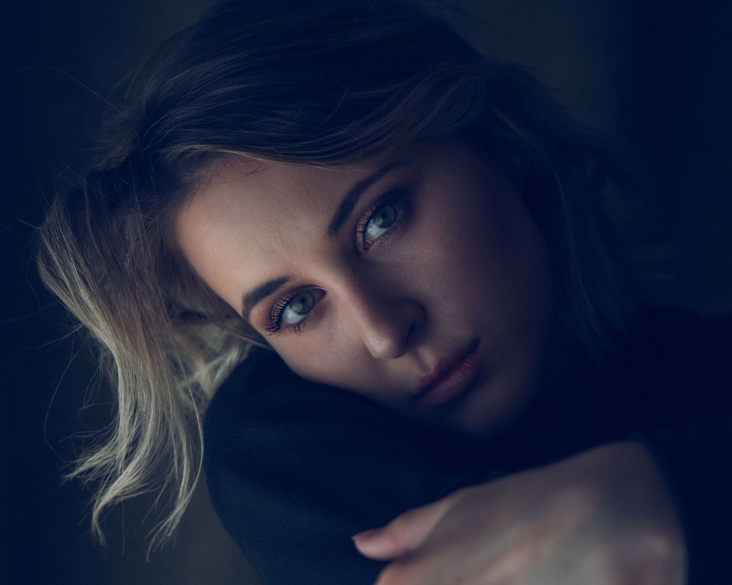 Artistic portrait series in dark moody lighting showing dramatic shadows and blonde hair against deep blue tones.