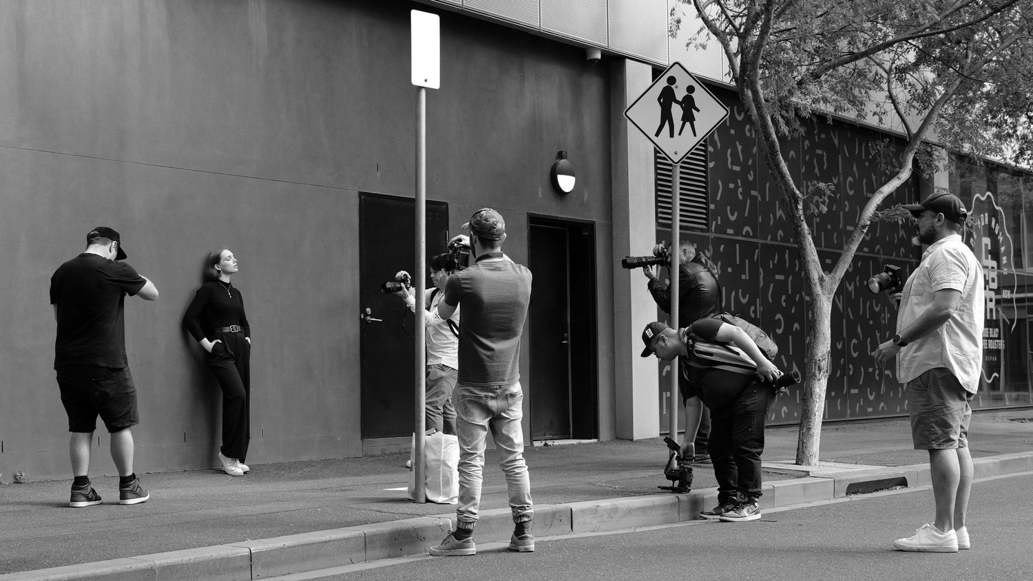 A black and white panoramic photograph showing several photographers taking photos of a model next to a building exterior.