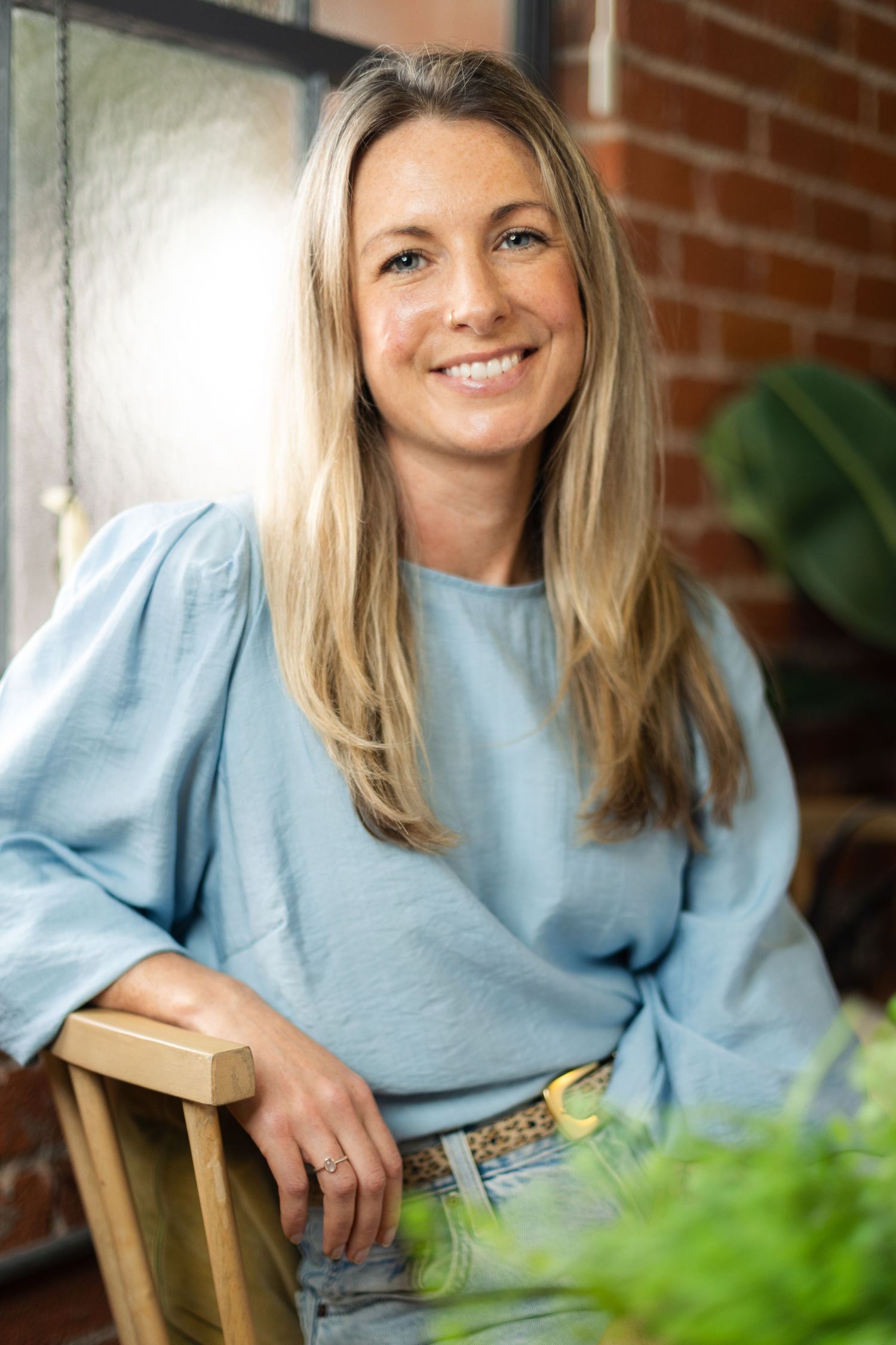 Person in light blue sweater sitting in wooden chair smiling at camera in sequence of four similar poses.