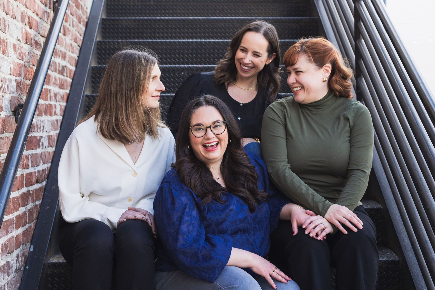 A group of people laughing and chatting while sitting on an outdoor metal staircase.