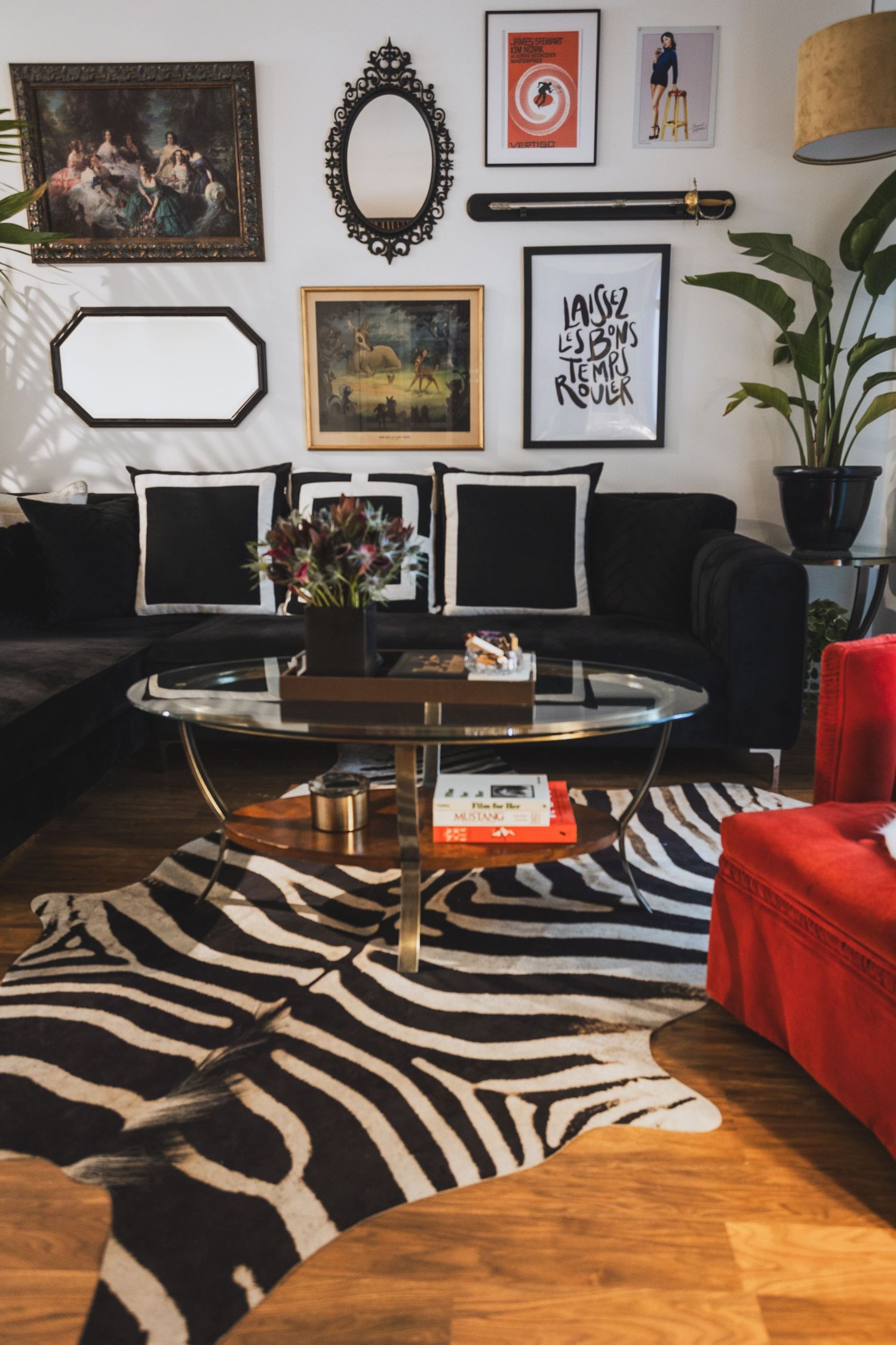 Eclectic living room with zebra rug, black velvet sofa, gallery wall, and glass coffee table on hardwood floors.