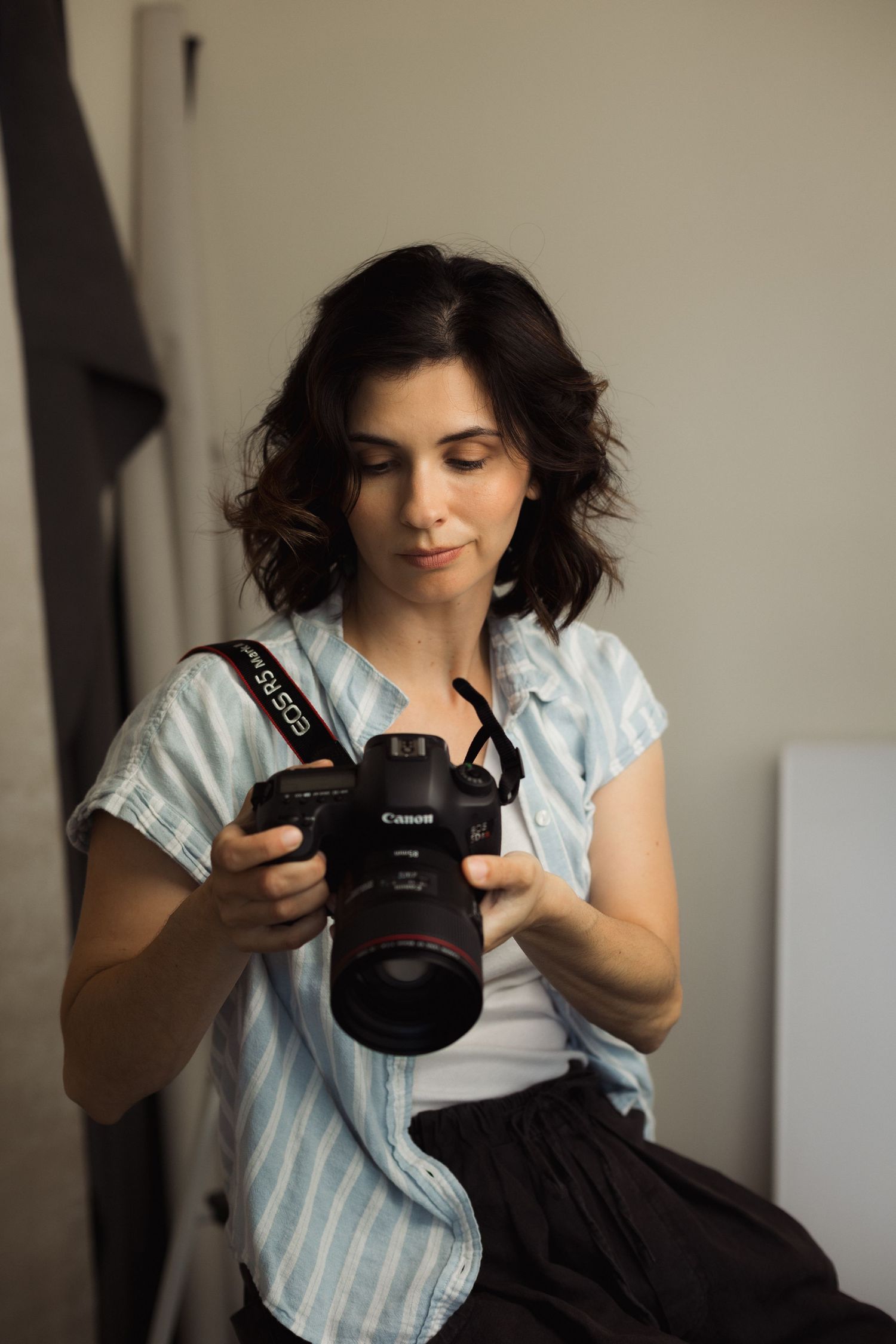Woman photographer reviewing shots on her Canon DSLR camera in a studio setting.