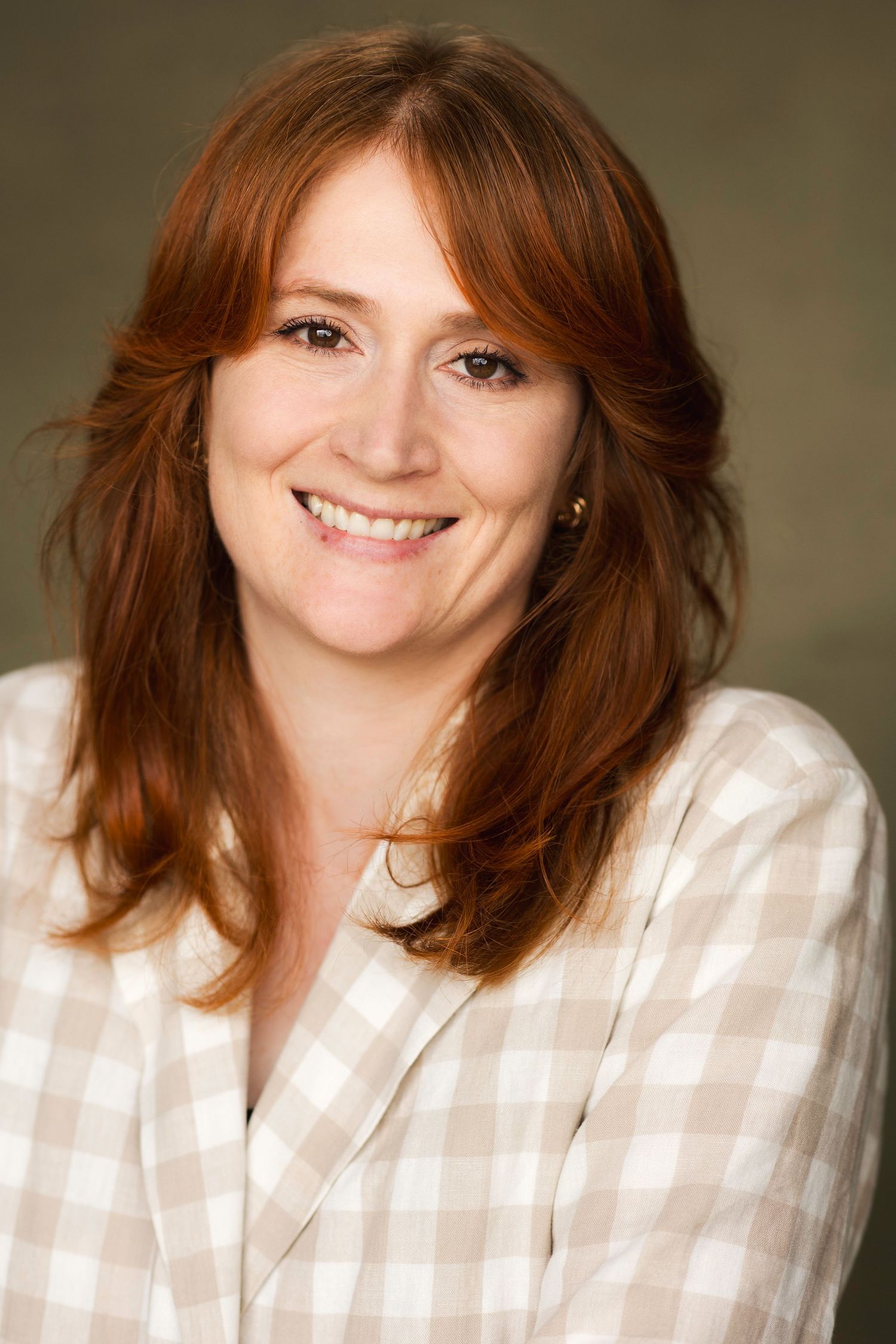 Smiling redhead woman in a plaid blazer poses for a professional headshot against a neutral background.