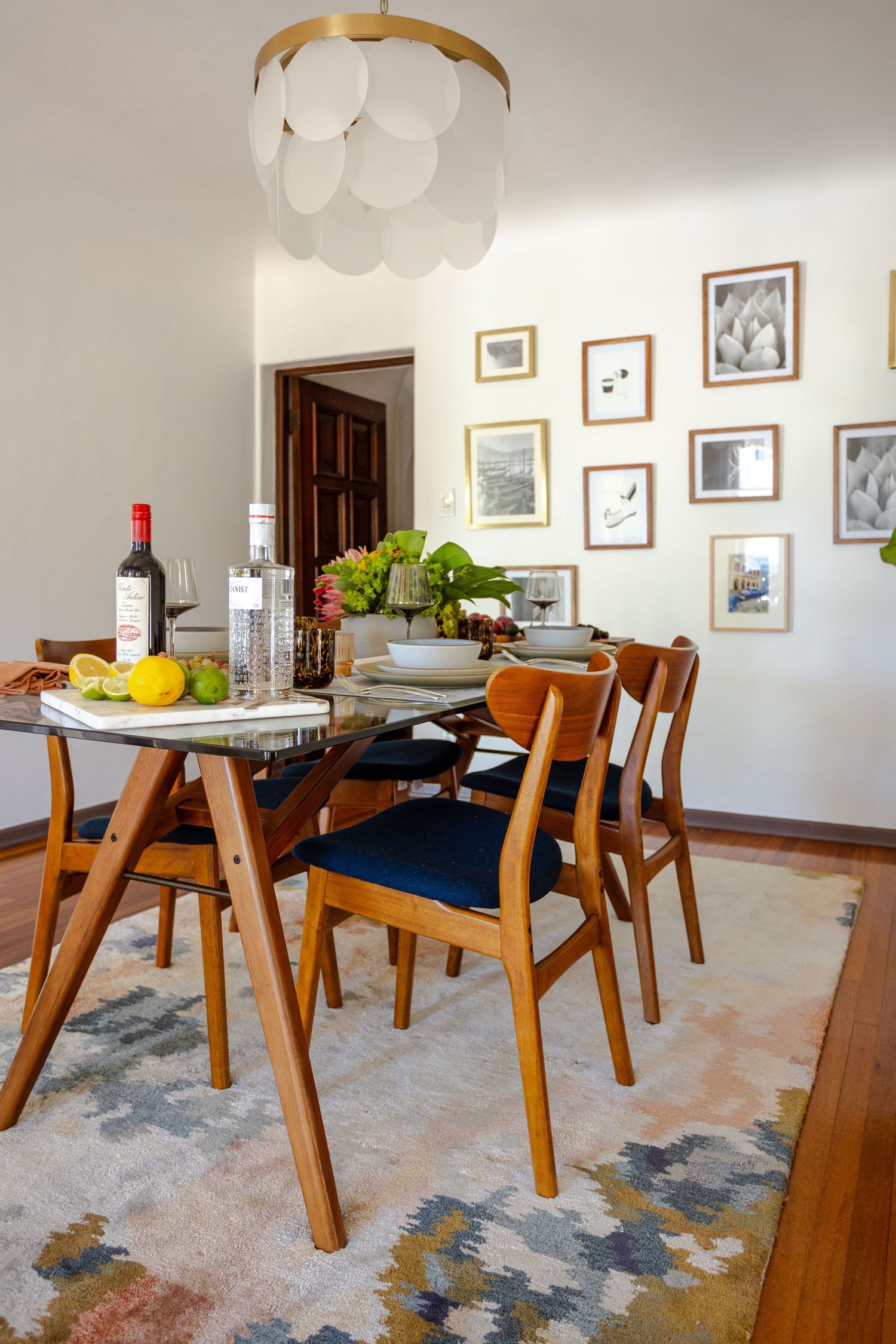 Mid-century modern dining room with wooden chairs, glass table, gallery wall, and elegant bubble chandelier.
