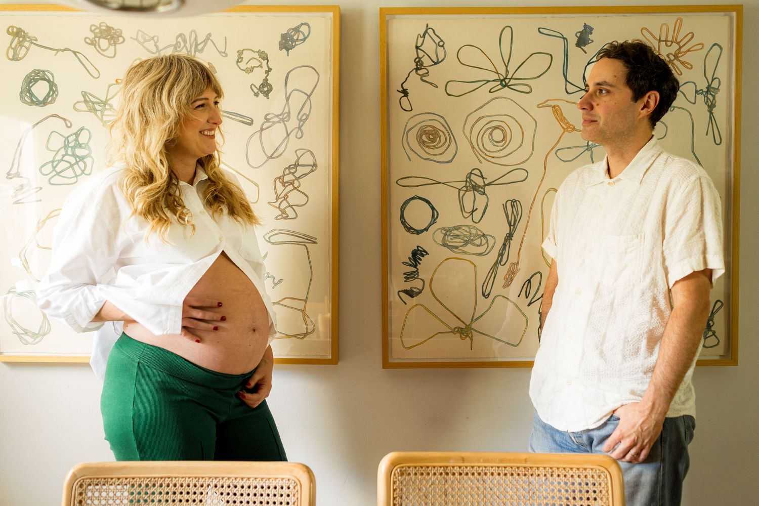 Artistic maternity photos taken against a wall with framed illustrations.