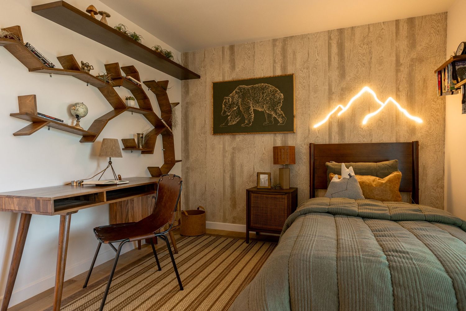 Nature-themed bedroom with tree bookshelf, striped rug, mountain neon light, wooden desk, and green textured bedding.