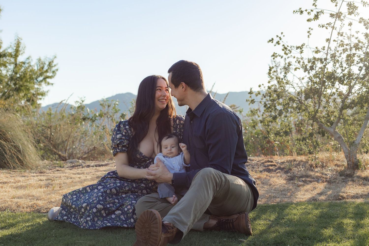 Couple sits together outdoors in natural lighting during golden hour photo session.
