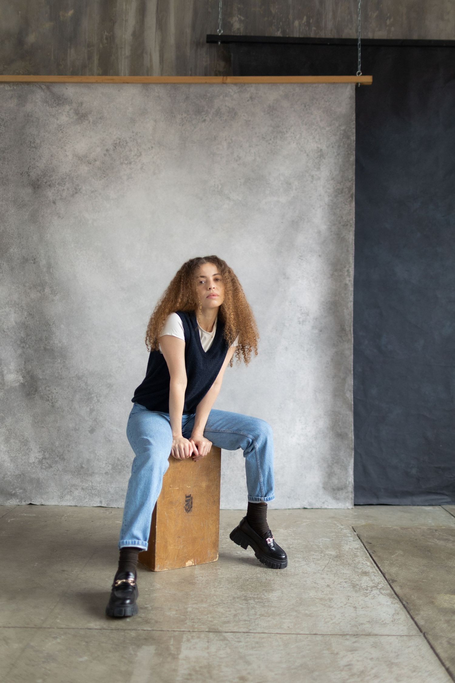 Person in casual attire poses with wooden box in industrial setting.