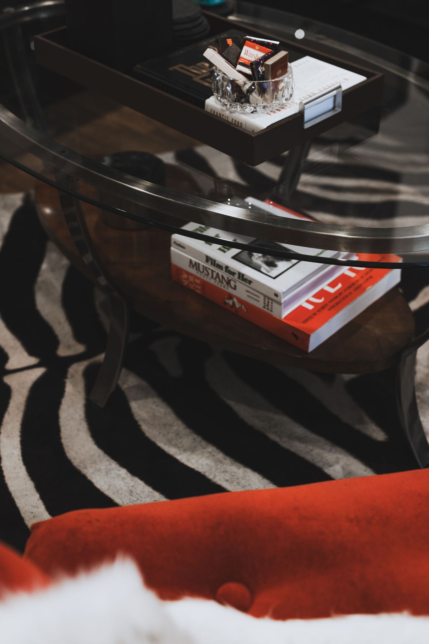 Glass coffee table with books including Mustang on zebra print rug, red sofa in stylish living room.