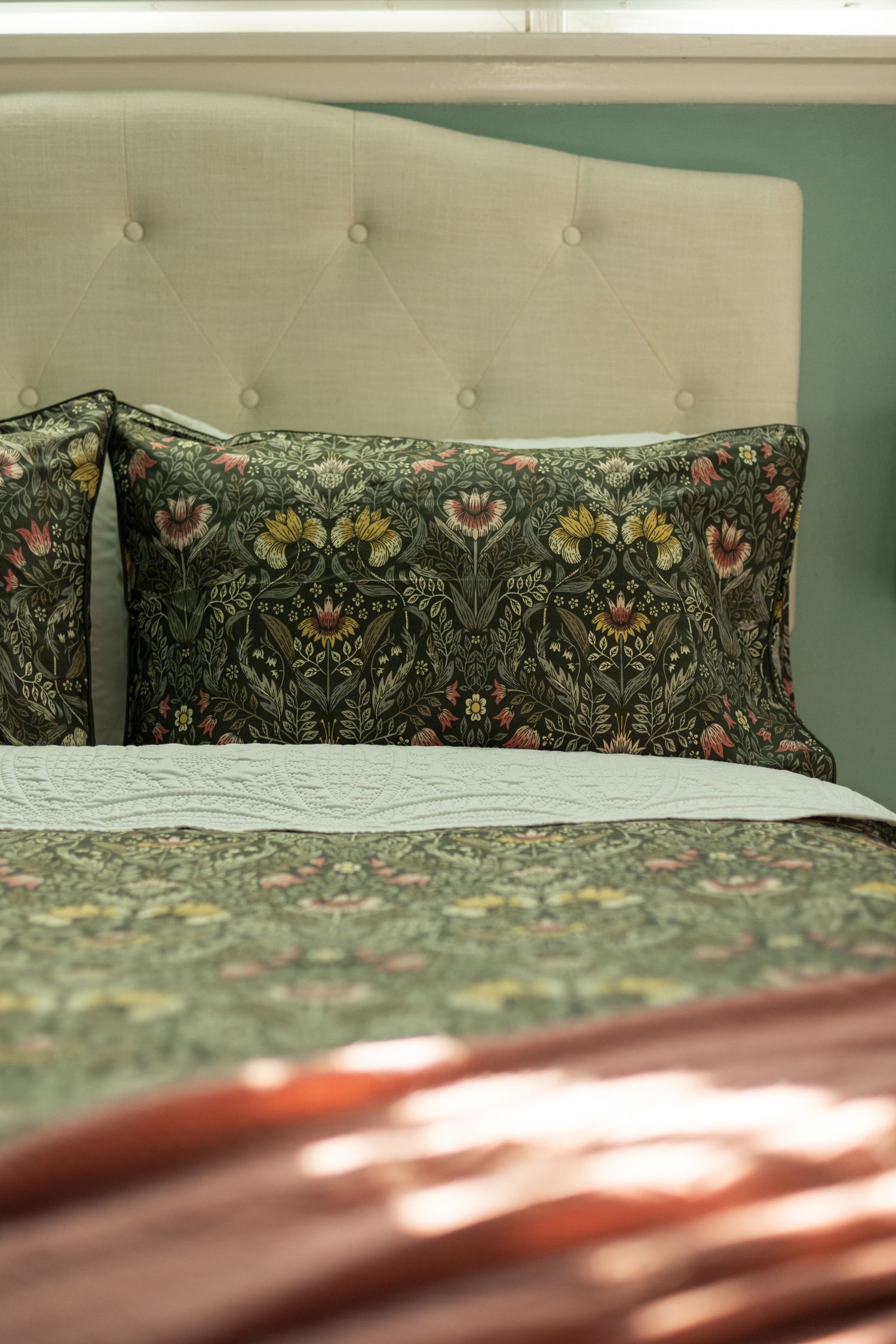 Tufted linen headboard with dark floral botanical patterned pillows and matching bedding in a serene bedroom.