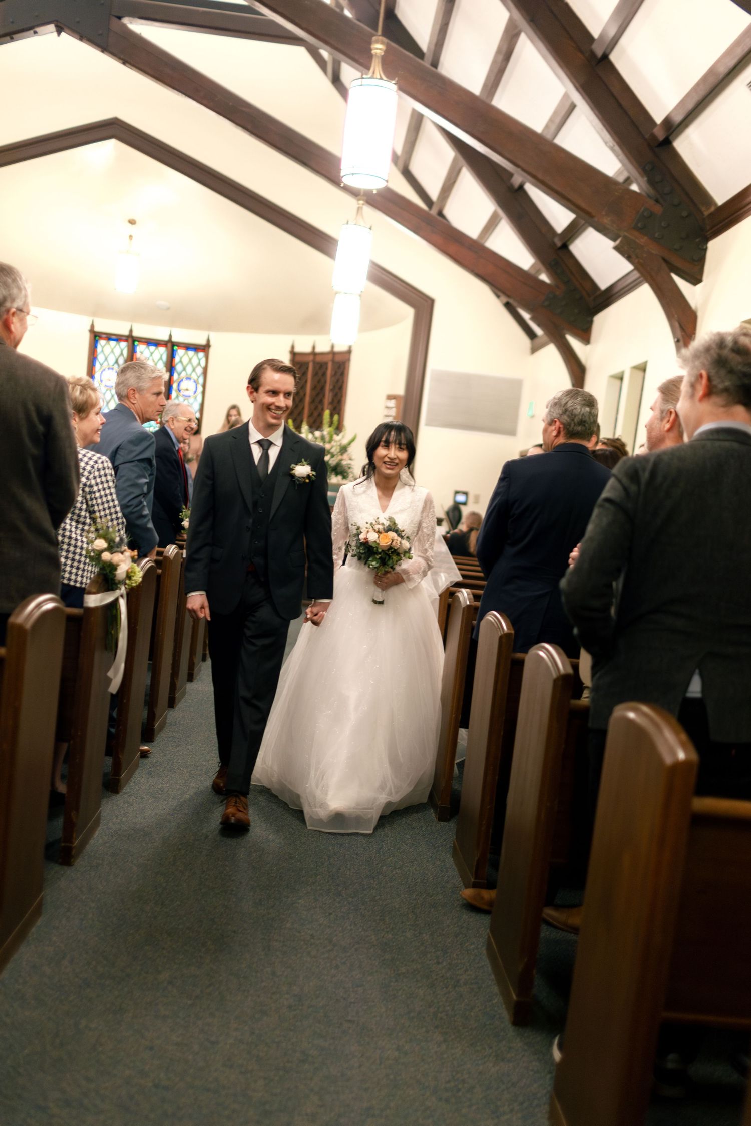 Wedding ceremony procession in a church with wooden pews and exposed beam ceiling.