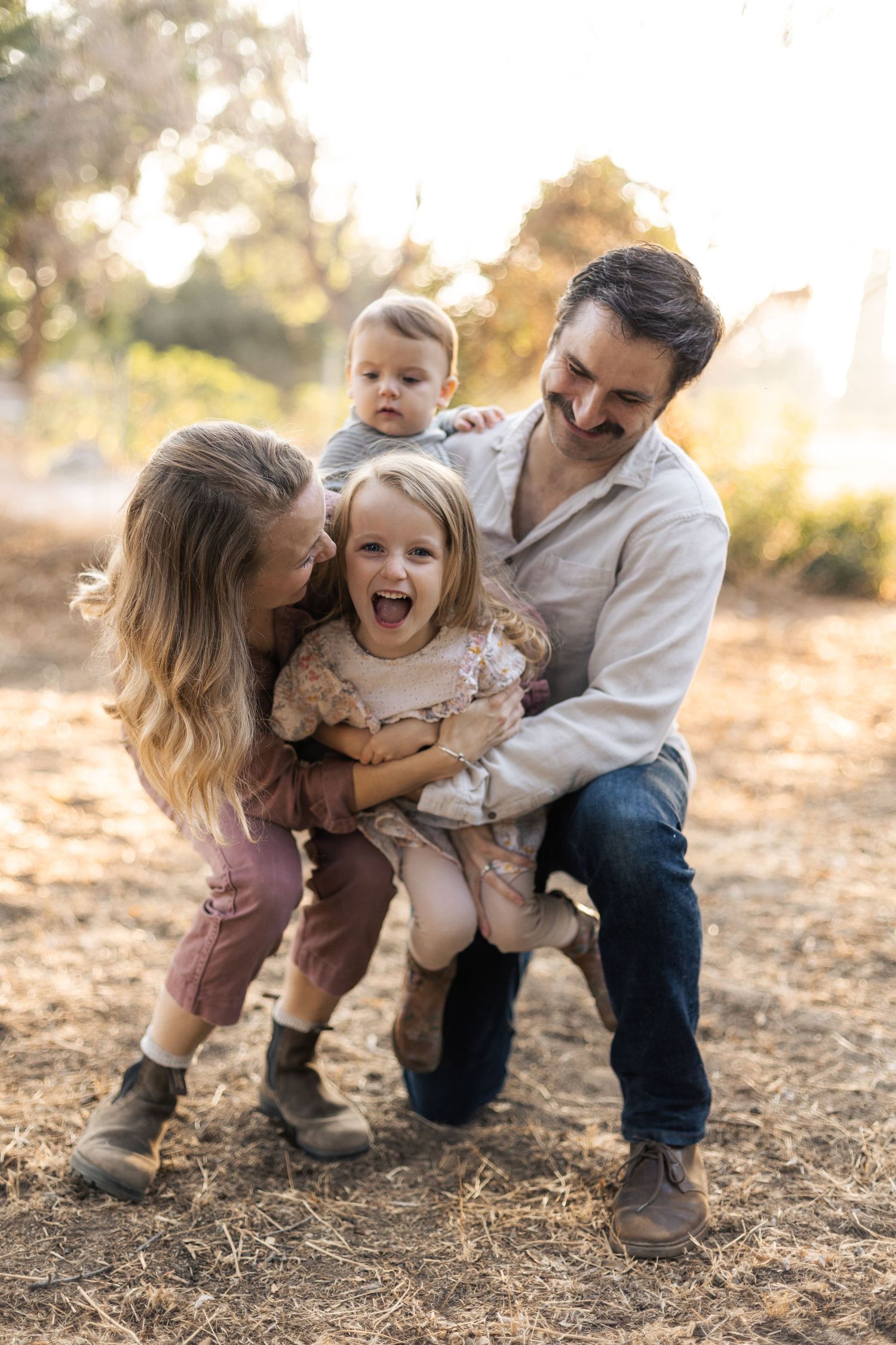 Playful family photography session captured at sunset in a rustic outdoor location.