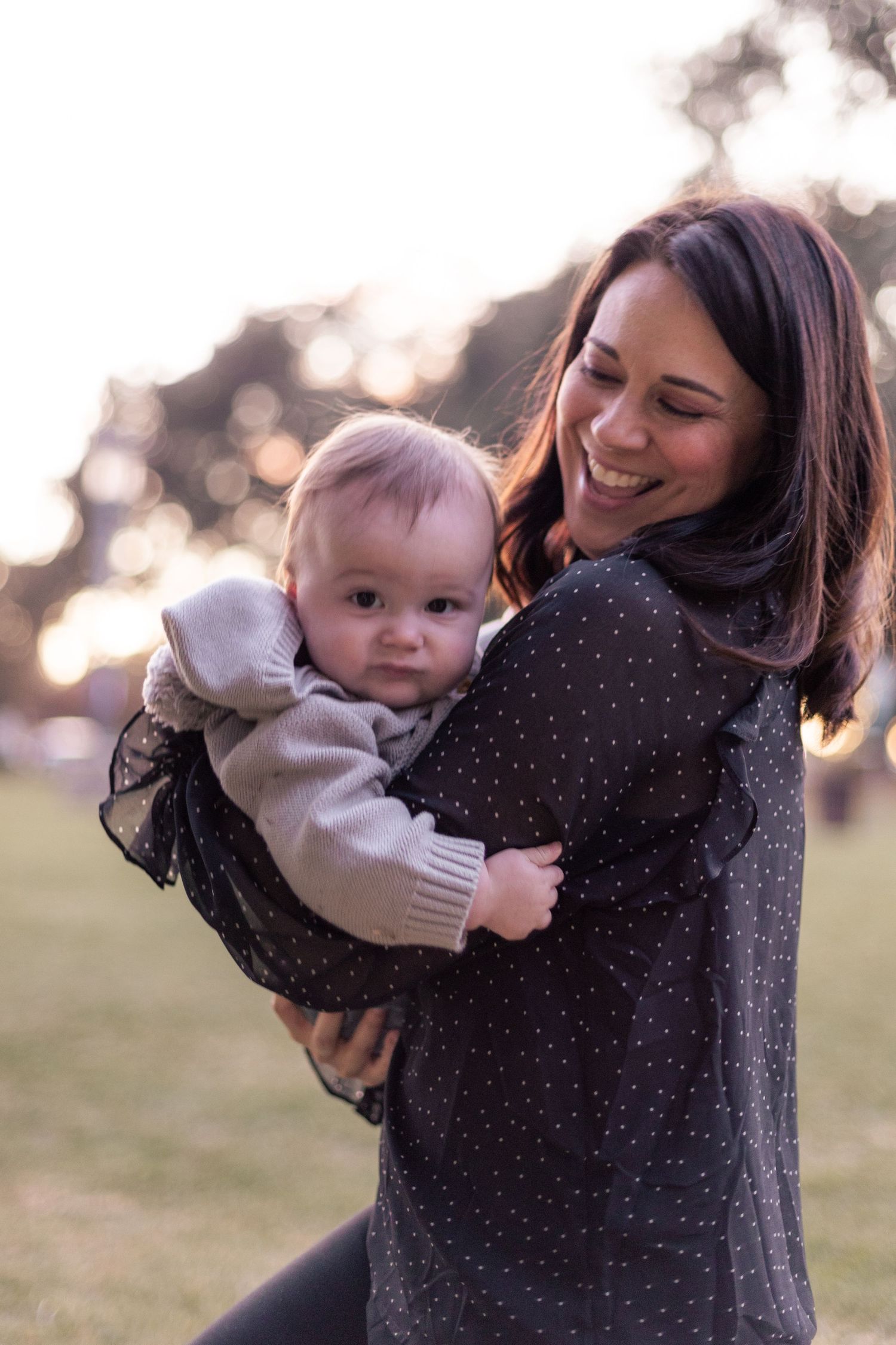 Playful moment with baby in white sweater against sunset backdrop.