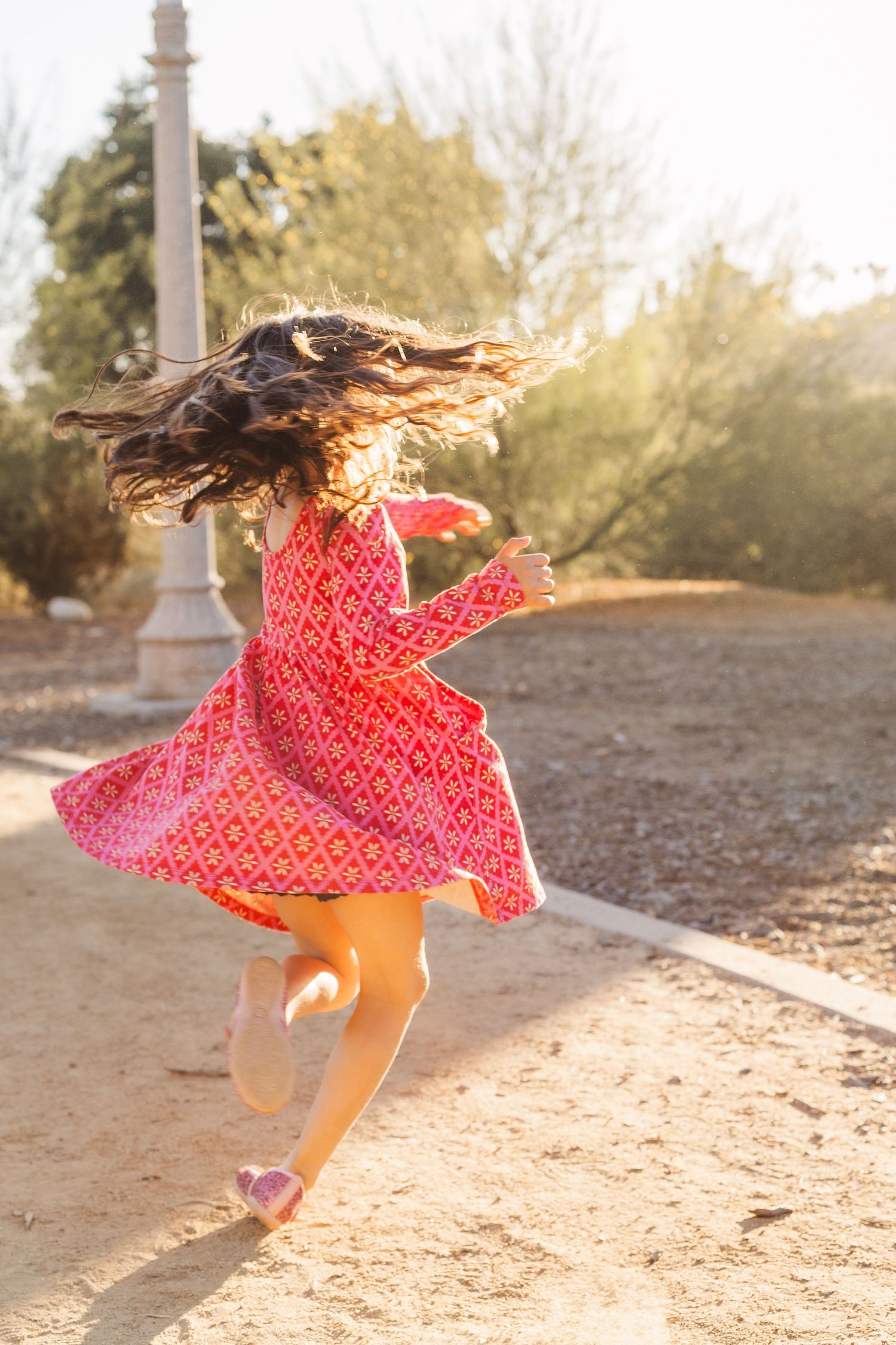 Young girl in red dress twirls and dances outdoors at sunset.