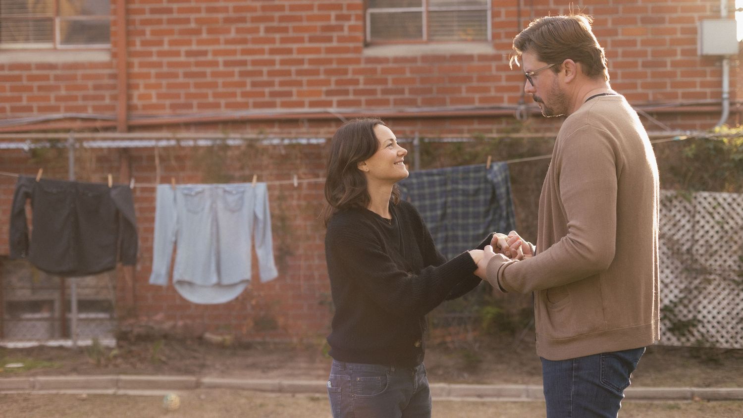 Couple shares romantic moments against brick wall background.
