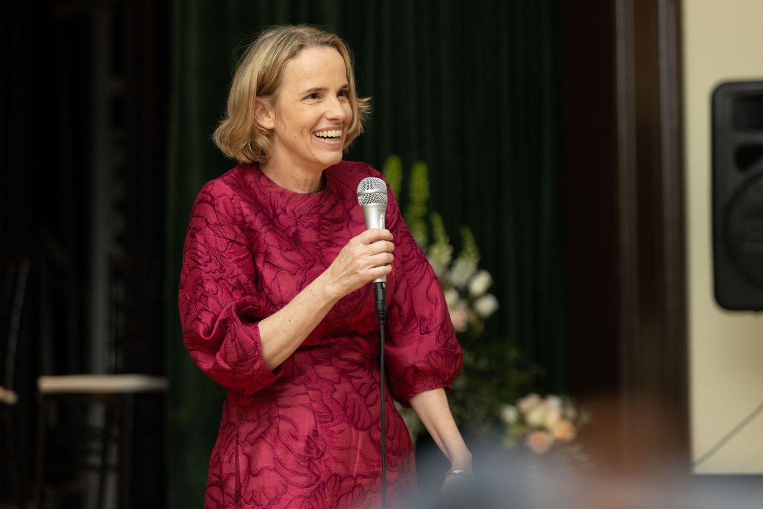 Speaker in a burgundy dress presenting at an indoor event.