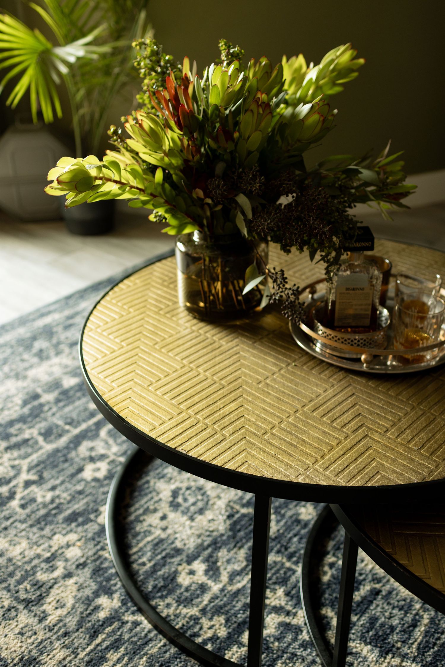 Gold geometric patterned coffee table with floral arrangement and tea set on blue vintage rug.