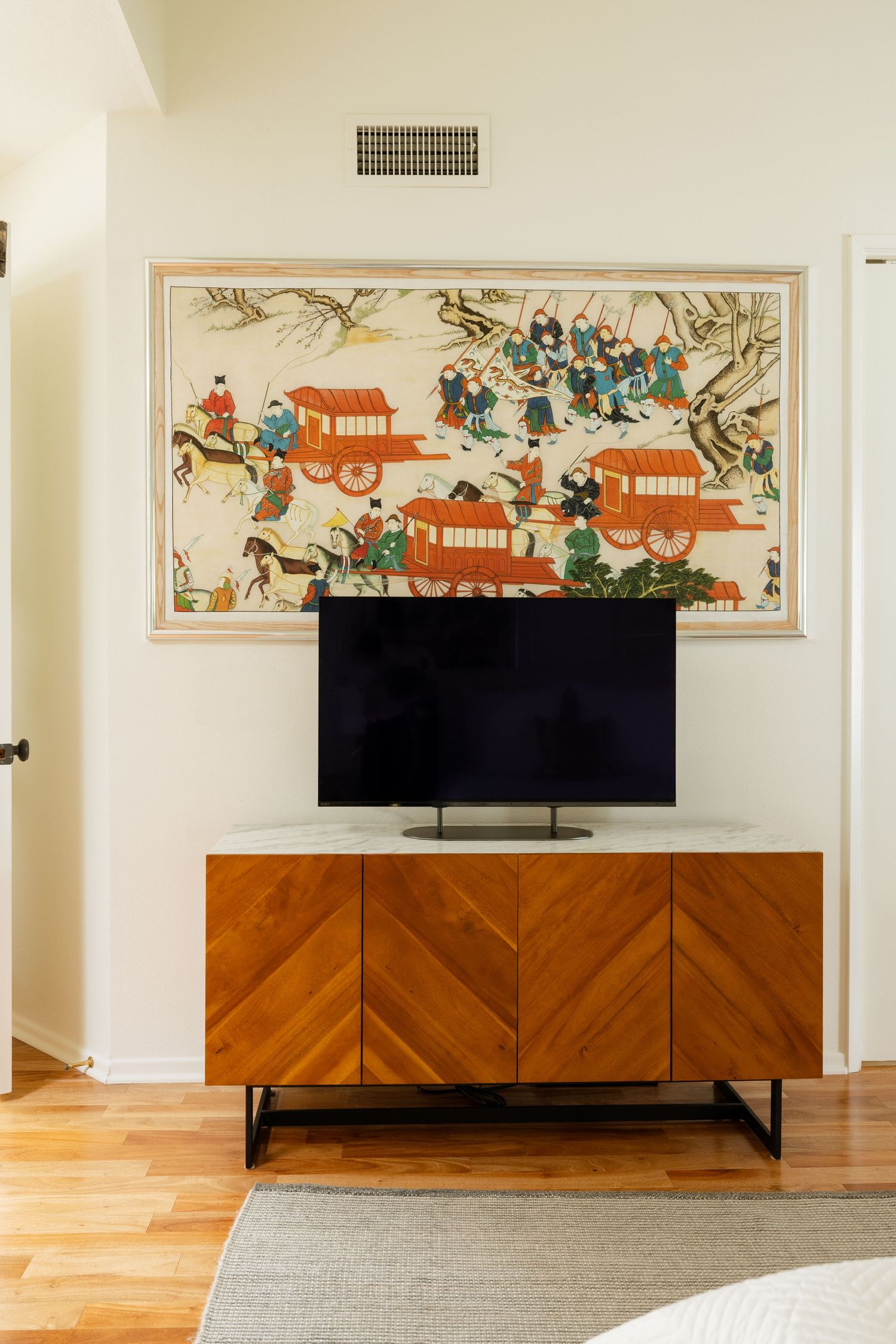 Mid-century modern wood chevron TV console with flat screen TV and Asian art painting on white wall.