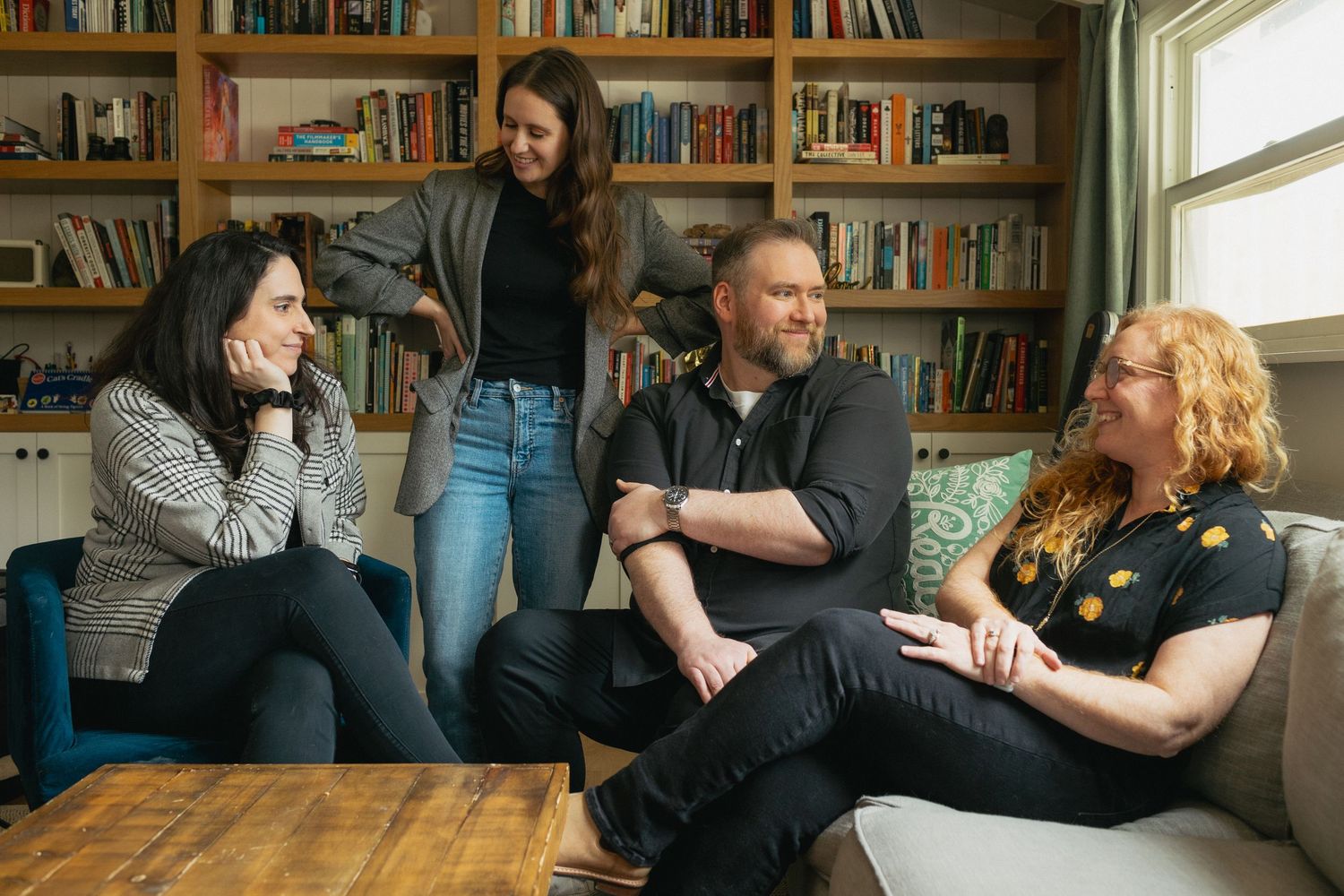 People sitting casually in a room with bookshelves and a window.