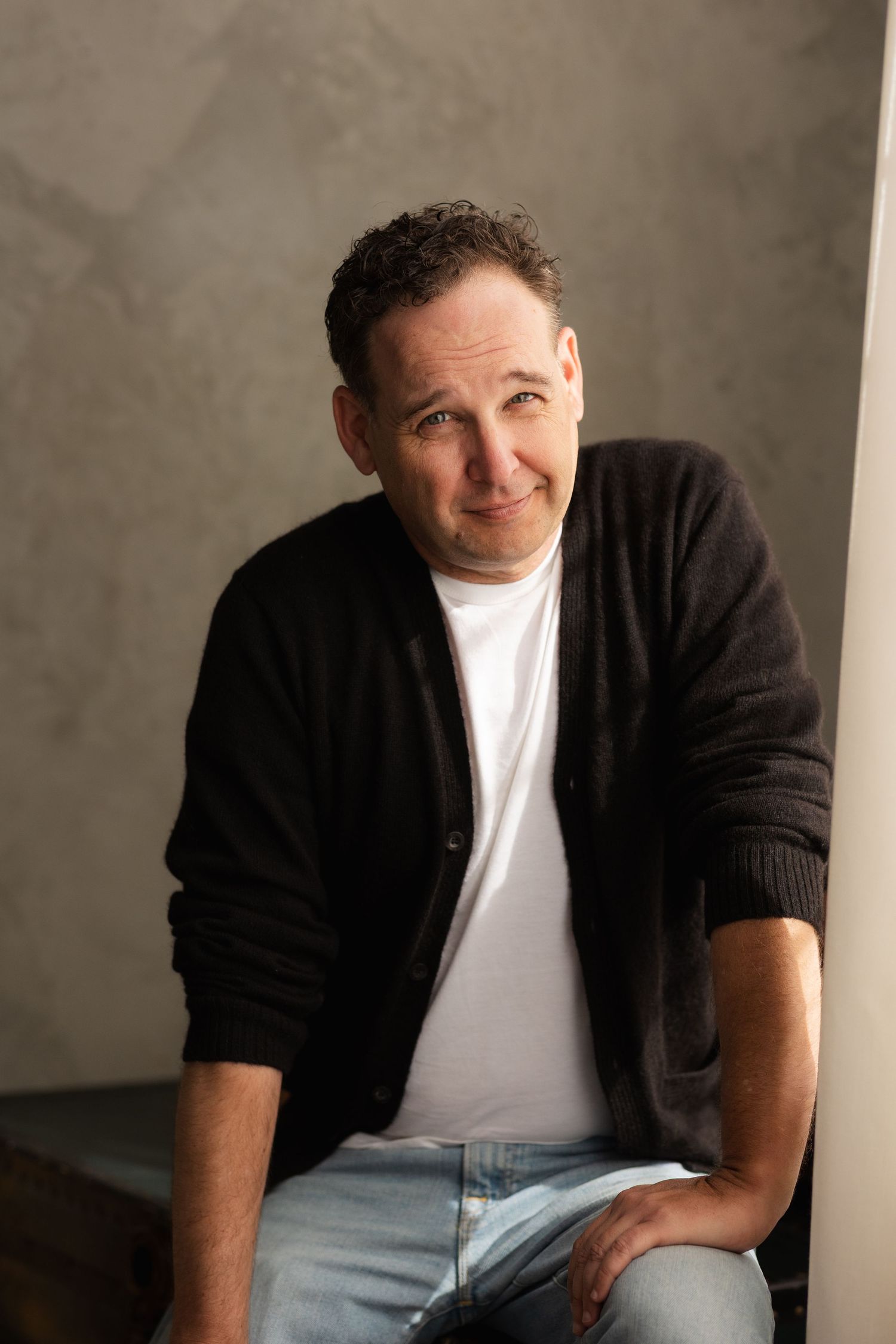 Person in black cardigan and white t-shirt sitting casually during studio photoshoot.
