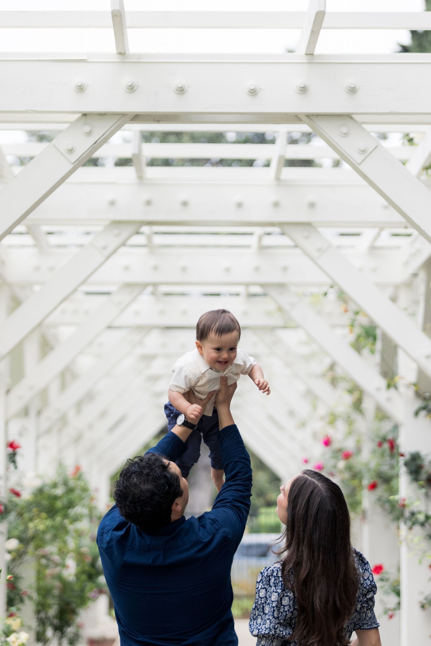 Sweet family moment under a white pergola surrounded by blooming roses.