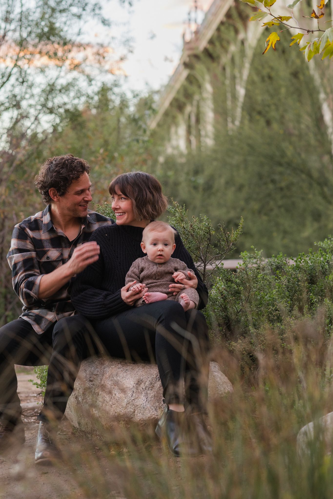 A family sits together on rocks outdoors with autumn foliage in the background.