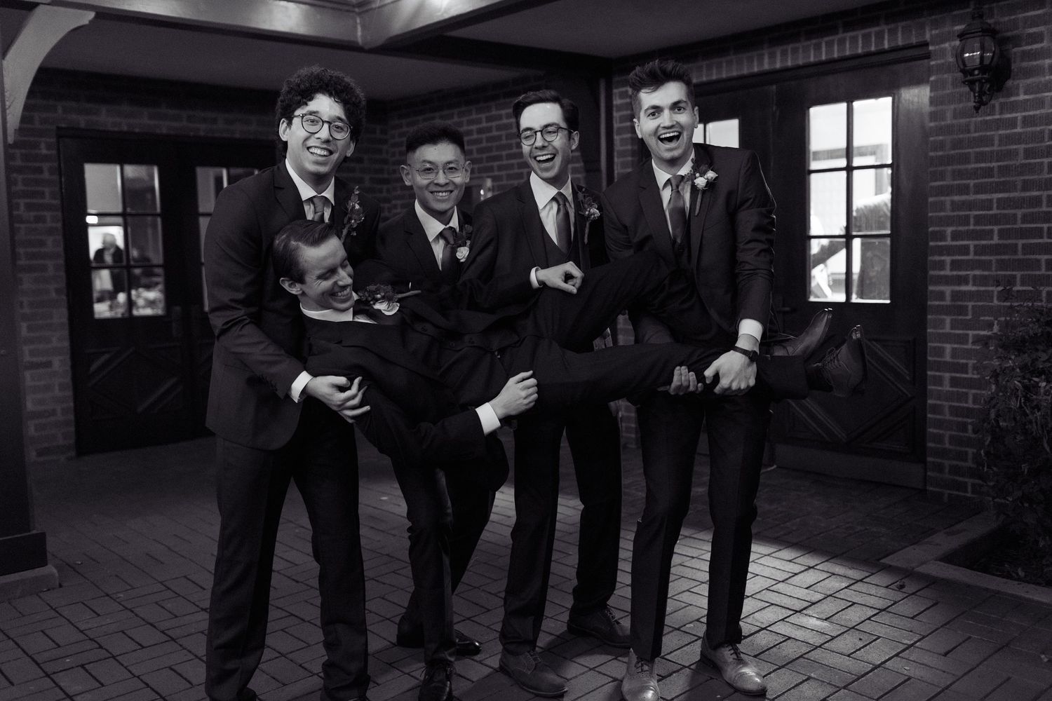 Wedding party in formal attire posing against brick exterior wall.