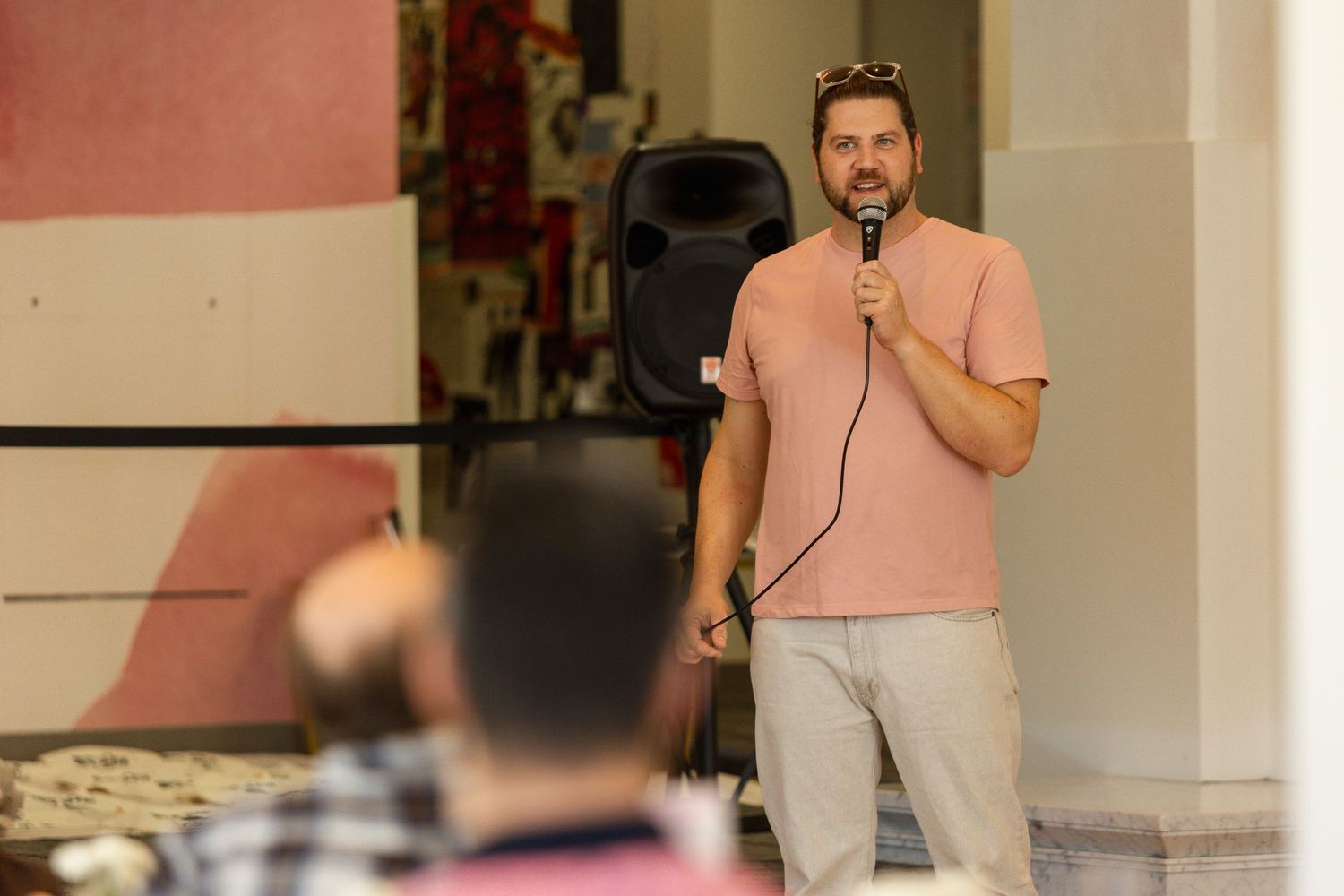 A person in a peach-colored shirt speaks into a microphone while standing on stage during a performance.