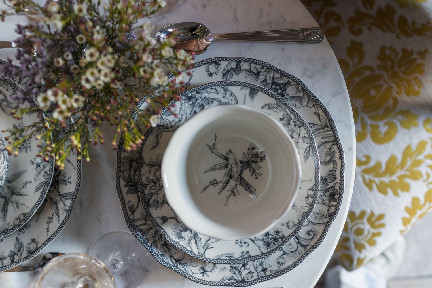 Elegant blue and white toile dinnerware set with floral arrangement on marble table.