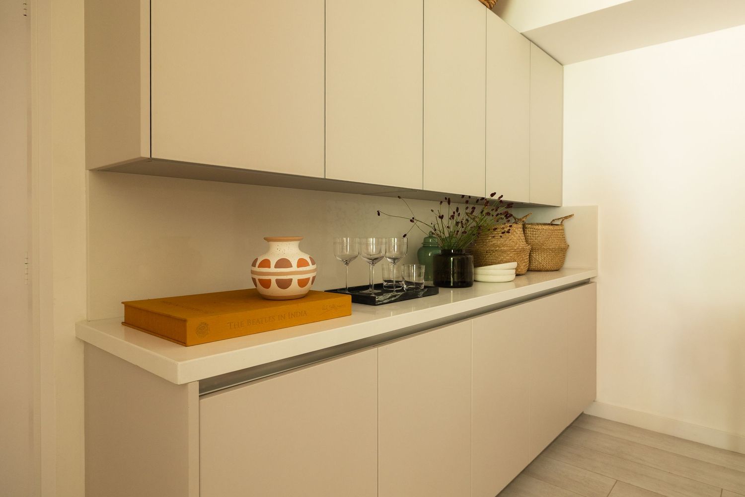 Modern white kitchen cabinets with minimalist design, featuring decorative items on a sleek countertop.