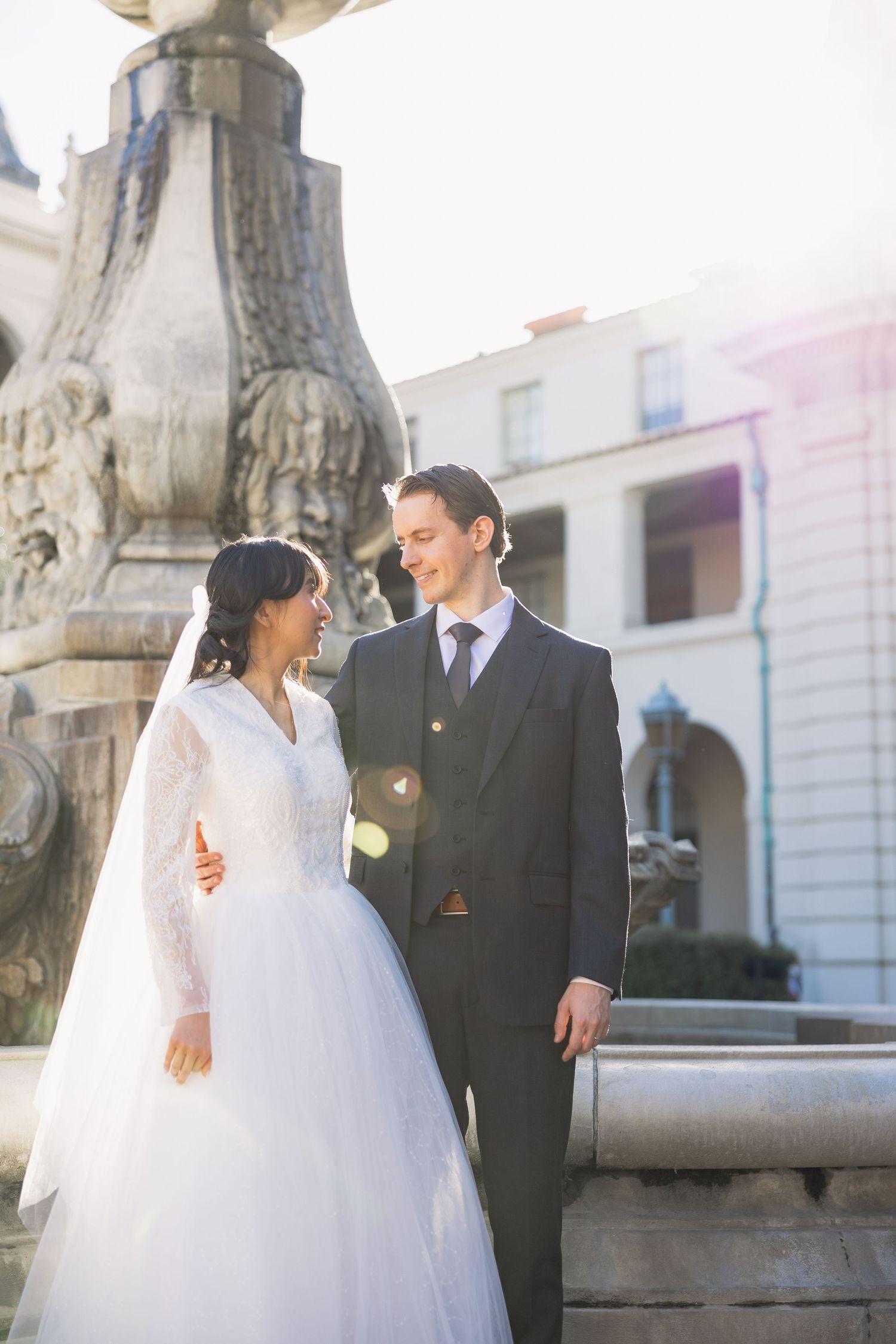 A romantic wedding portrait by an ornate fountain with the bride in a white gown and groom in a dark suit.