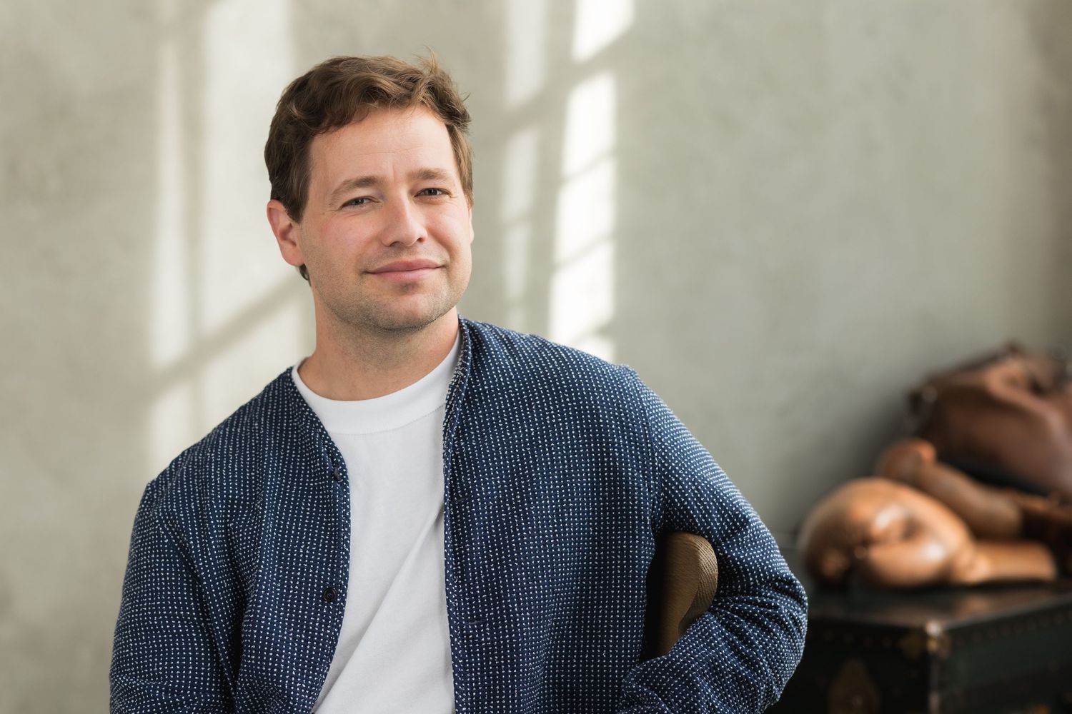 A person wearing a navy cardigan and white t-shirt poses in front of a sunlit wall.