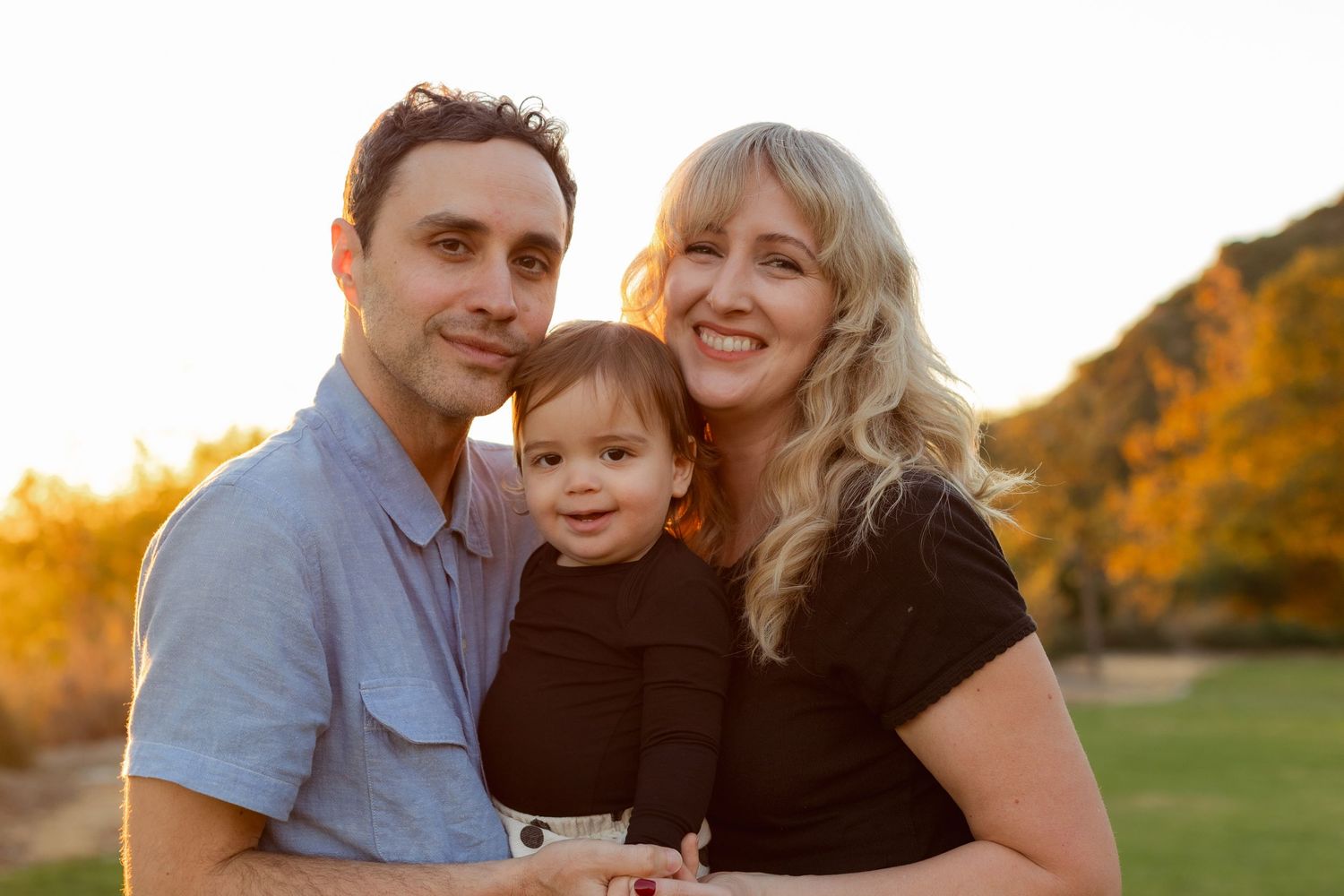 Candid family portraits taken at sunset in a grassy field with golden autumn colors in the background.