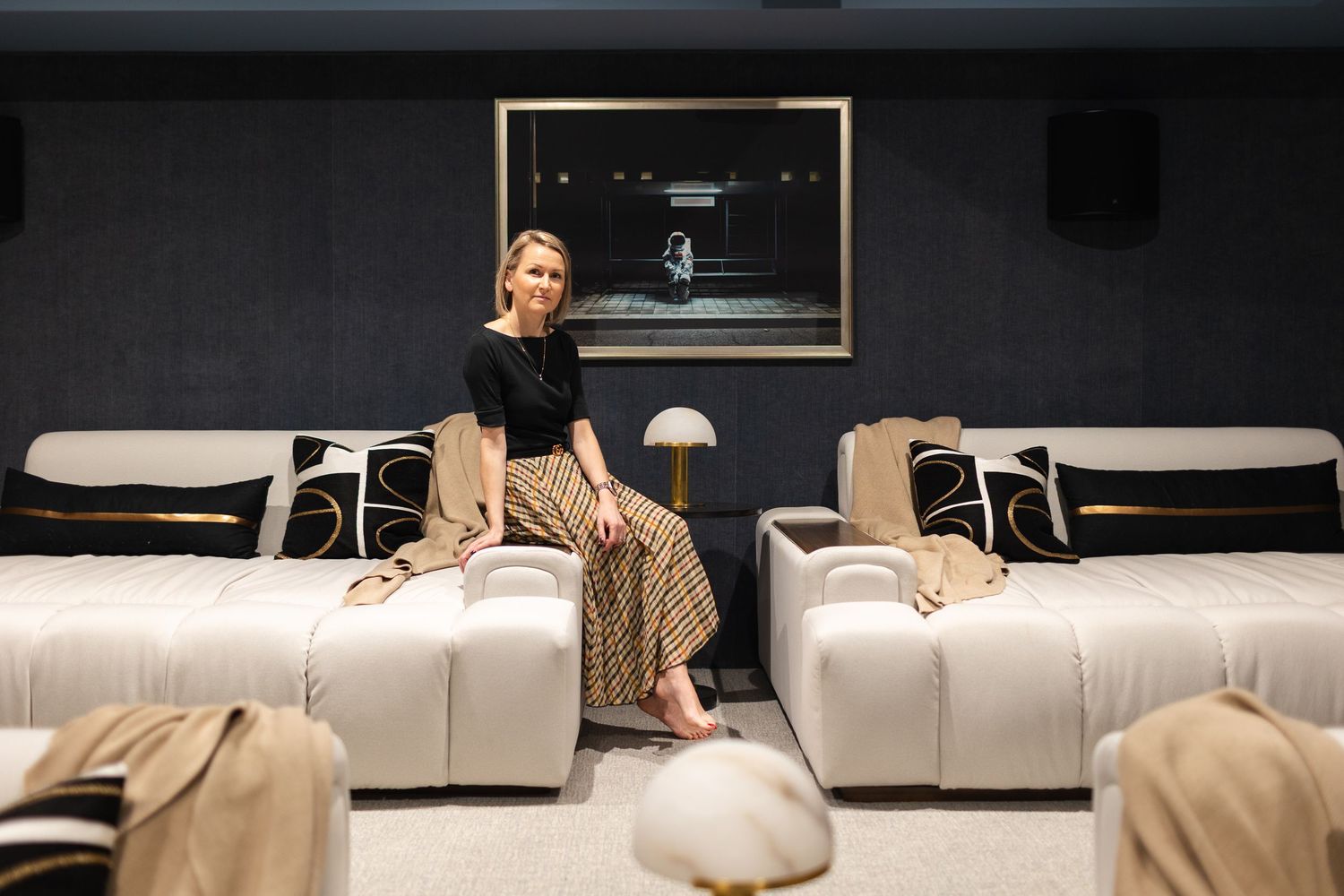 Woman sitting in a luxurious home cinema room with cream sofas, dark walls, and a large screen.