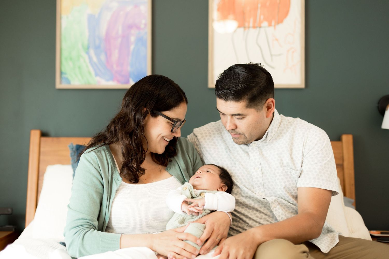 Tender indoor family moment with a baby against a sage green wall with colorful artwork.